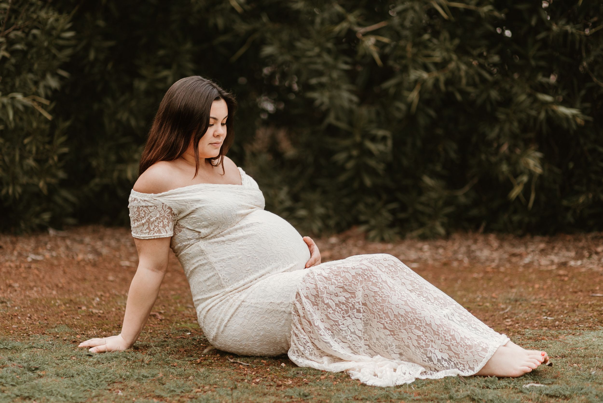 Ethereal maternity photoshoot in a garden setting with flowing white lace dress.