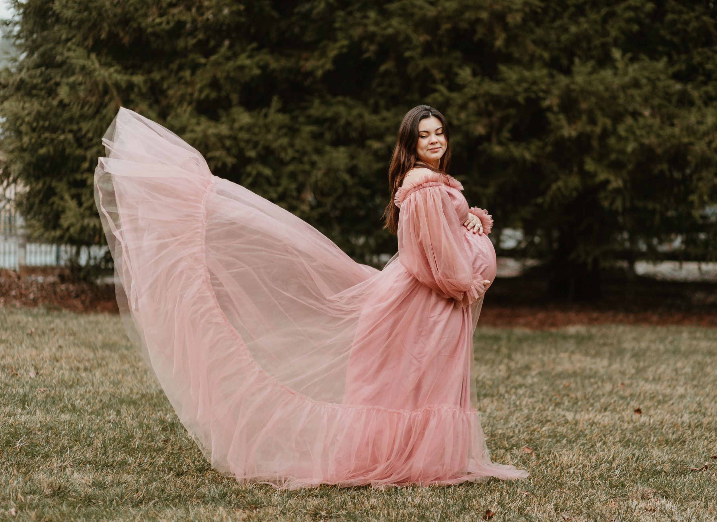 Romantic maternity session with billowing pink tulle dress in an outdoor setting.
