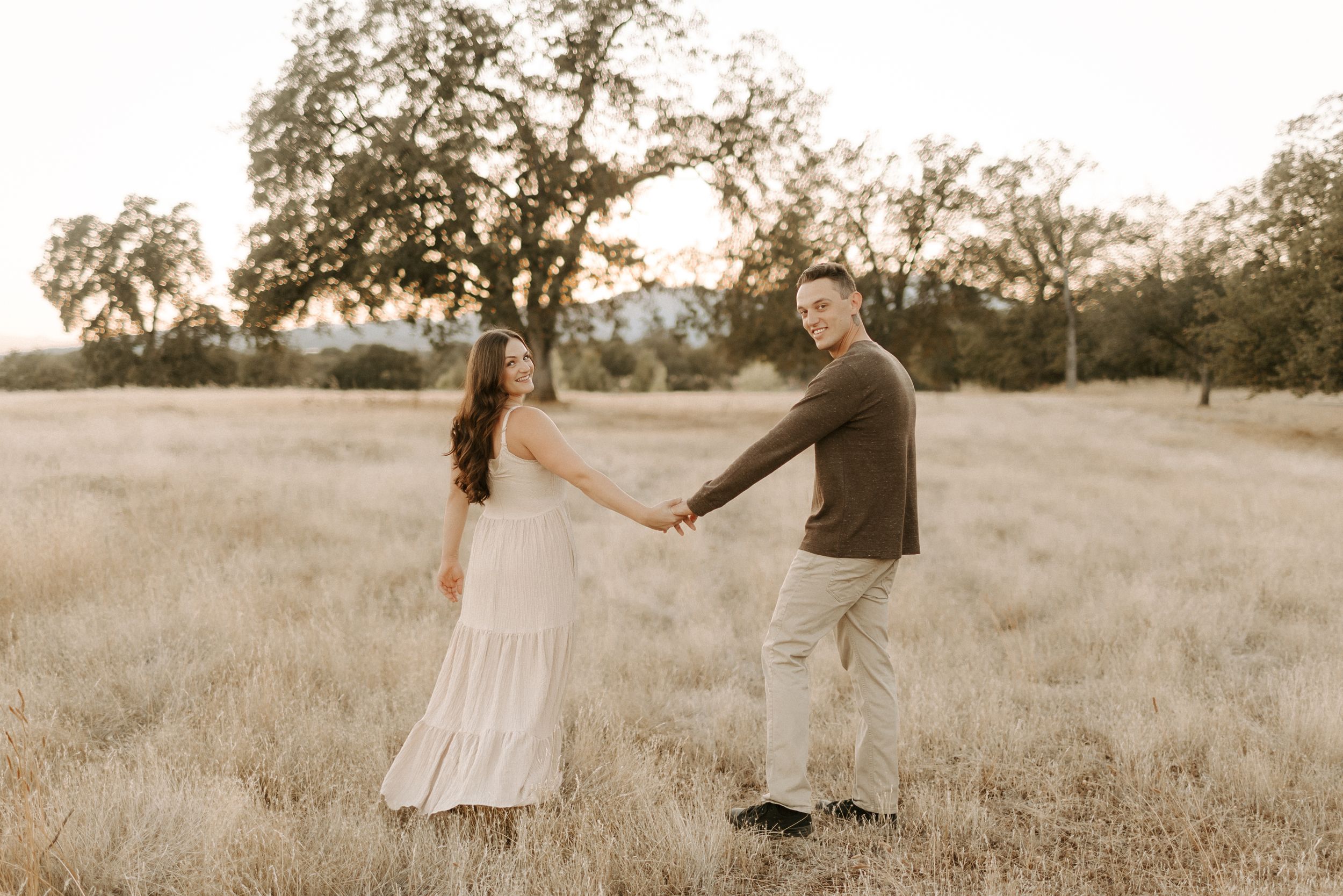 Natural lifestyle photography session in cream dresses among tall grass at sunset.
