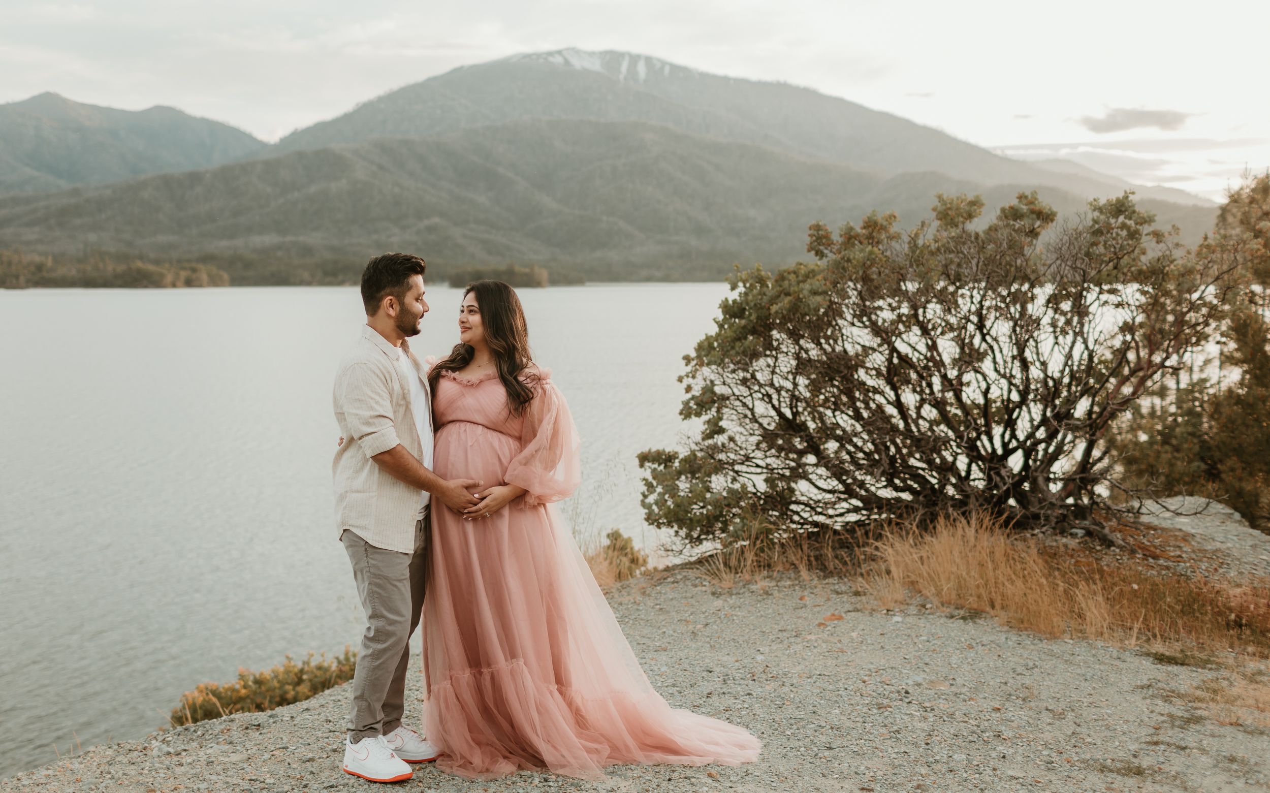 A romantic mountain lakeside photoshoot featuring flowing pink fabric against a natural backdrop.