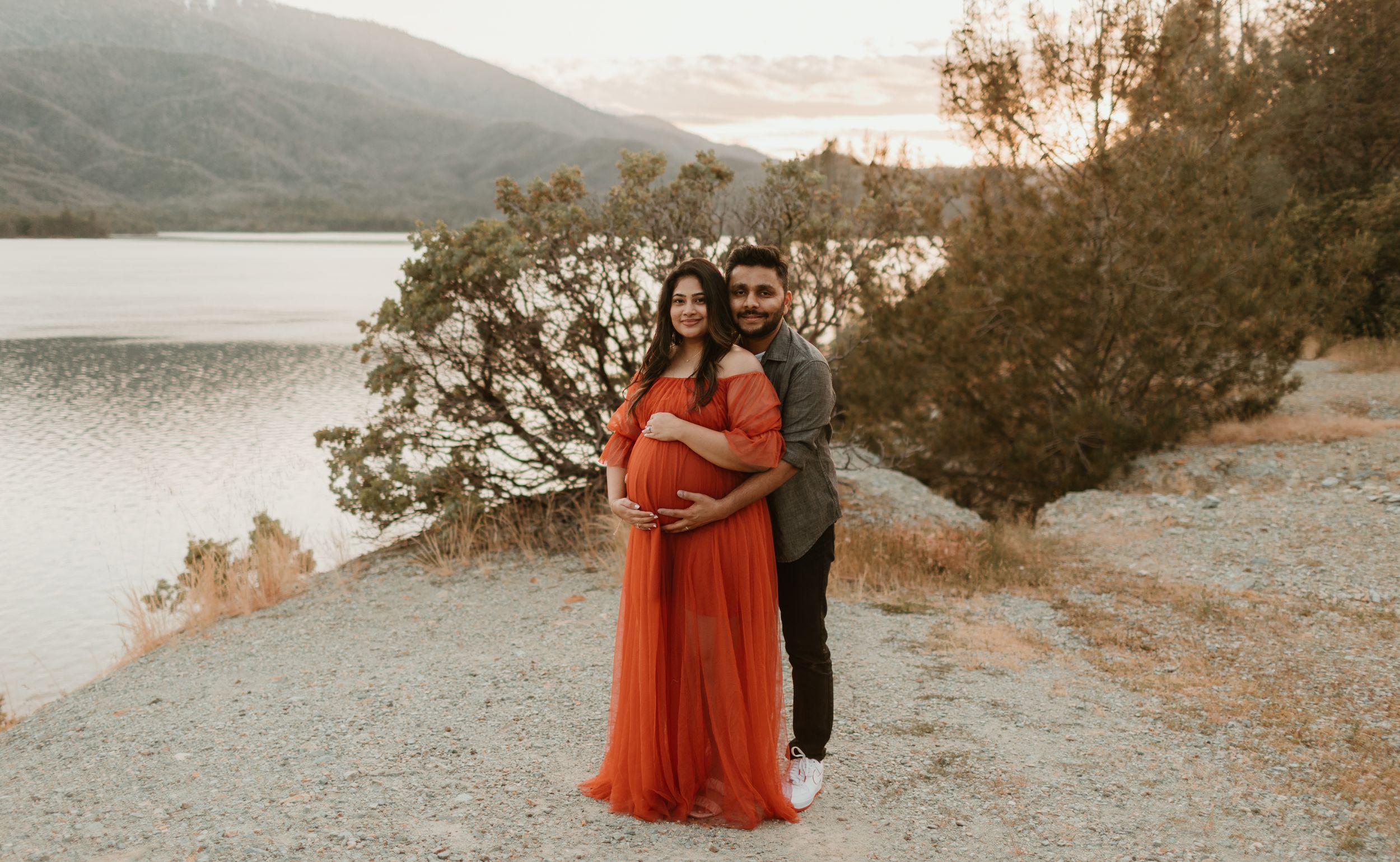 A vibrant red dress contrasts beautifully against a mountainous lake backdrop during golden hour.