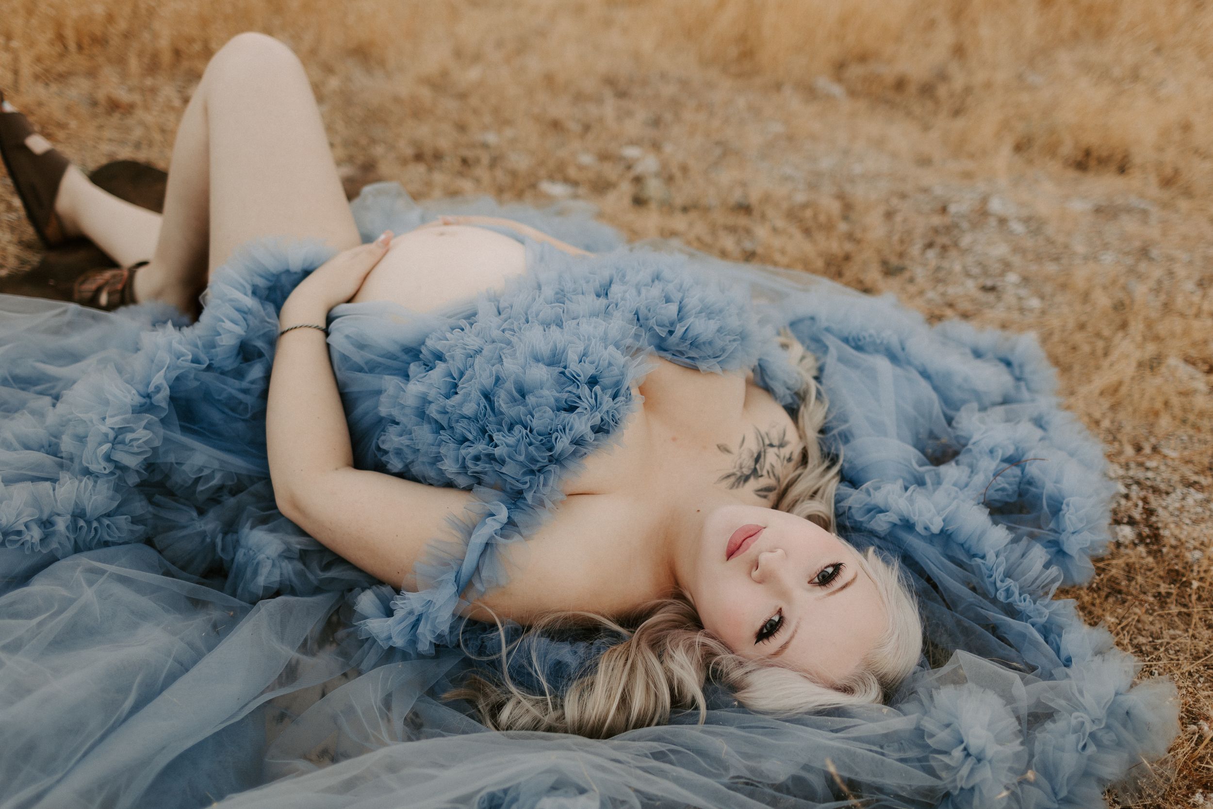 Dreamy portrait session featuring blue tulle gown against golden dried grass landscape.