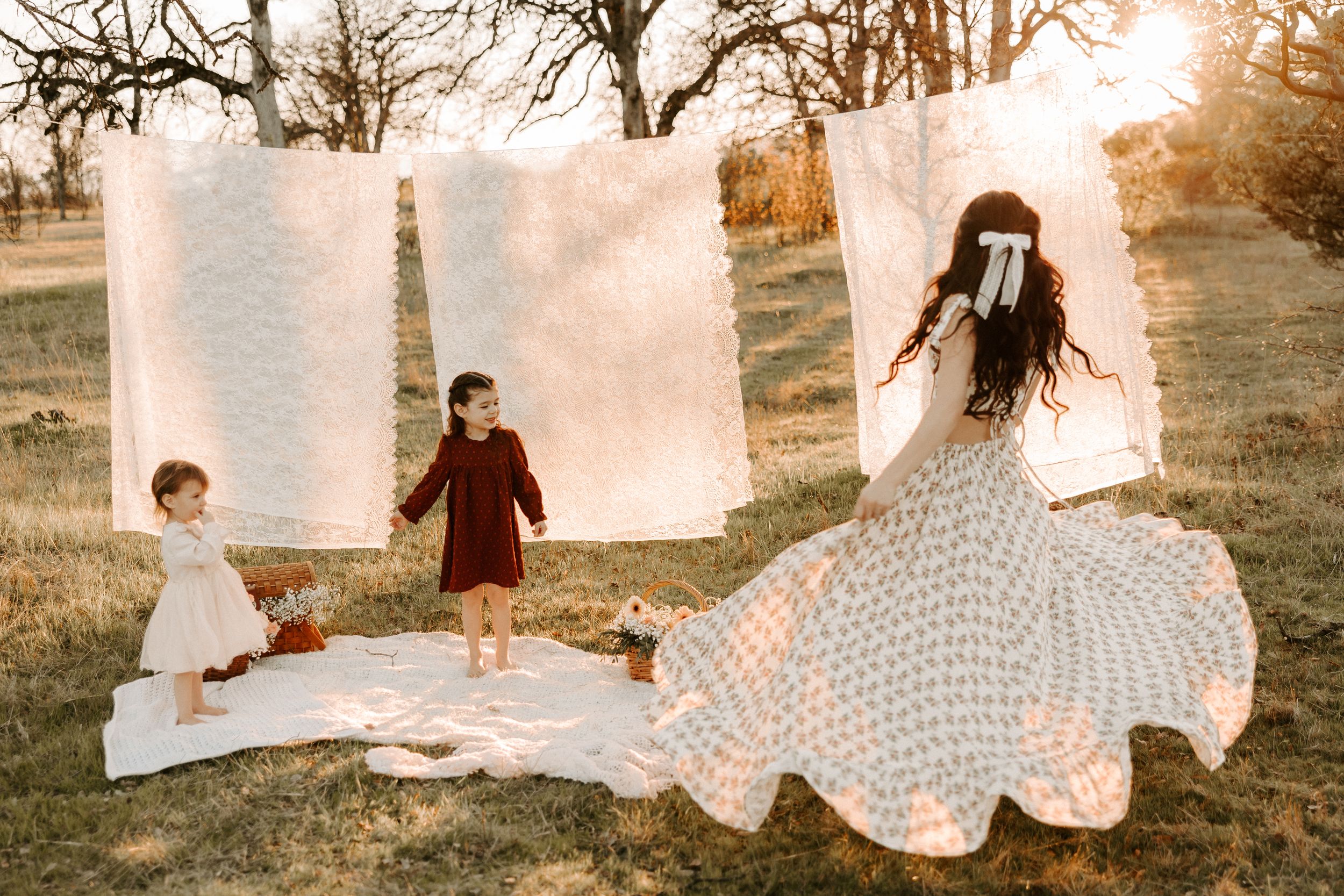 Ethereal family maternity session among hanging white linens at golden hour.