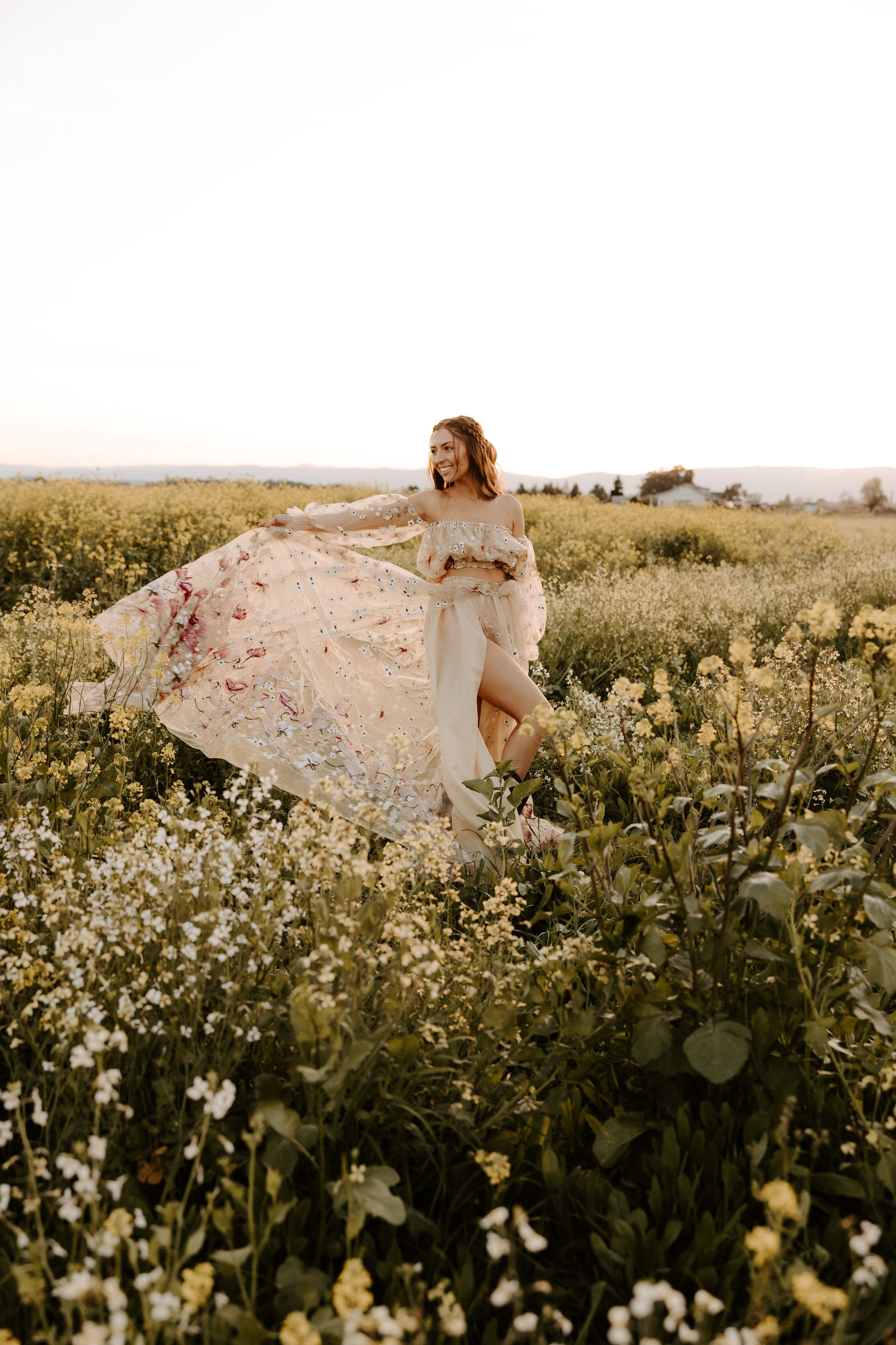 Whimsical maternity photography in a wildflower field with flowing pink dress at sunset.