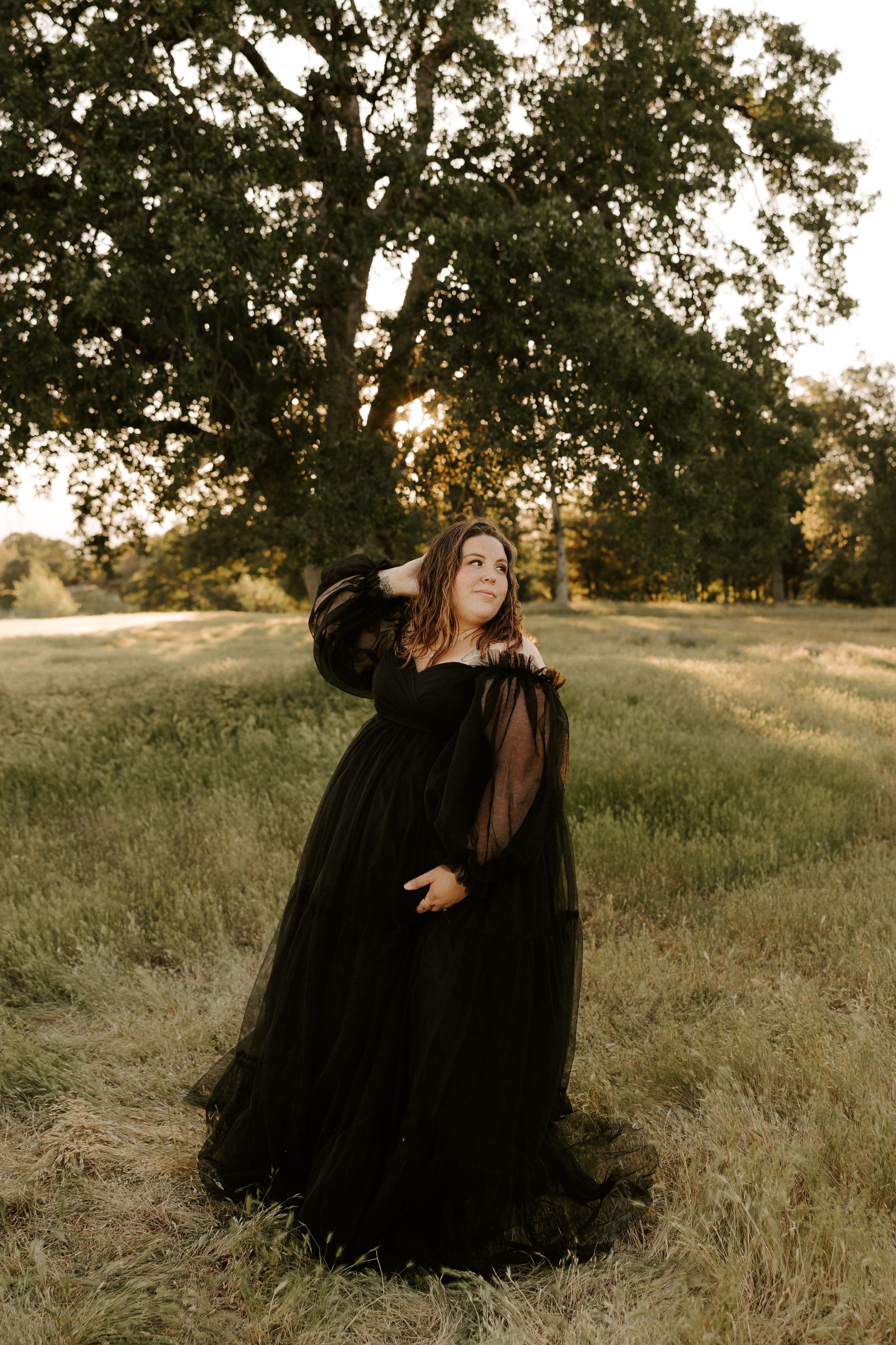 Artistic maternity portraits in a black tulle gown against golden hour lighting.