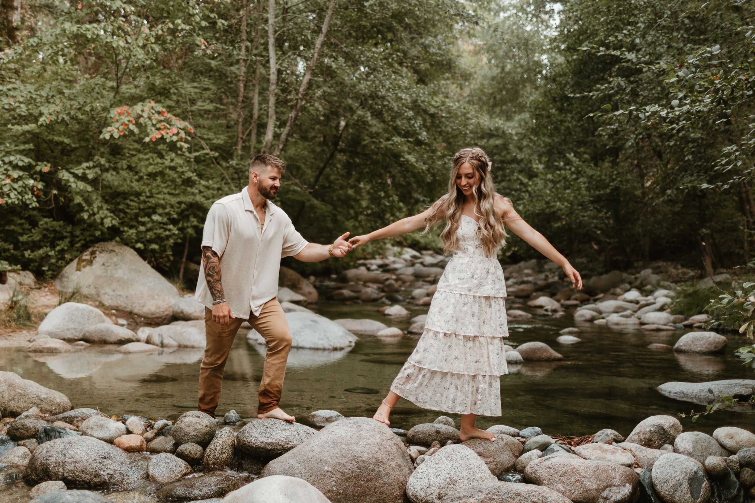 Playful couple session on rocky creek bed surrounded by lush greenery.