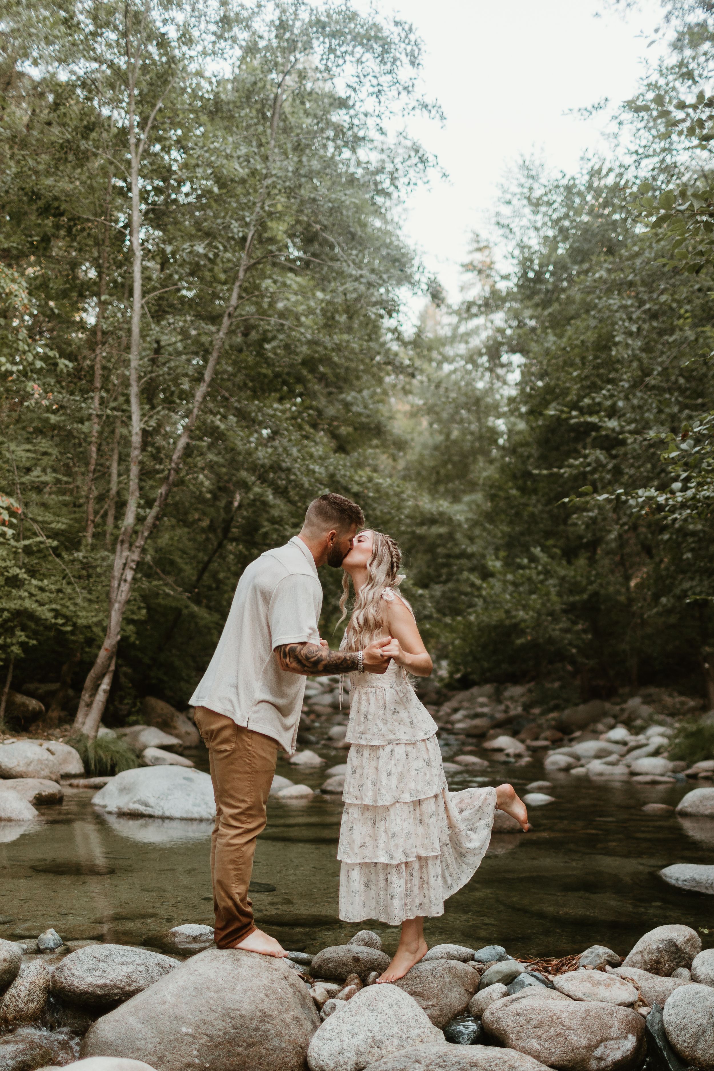 Romantic creek-side photo session with couple balancing on rocks in natural setting.