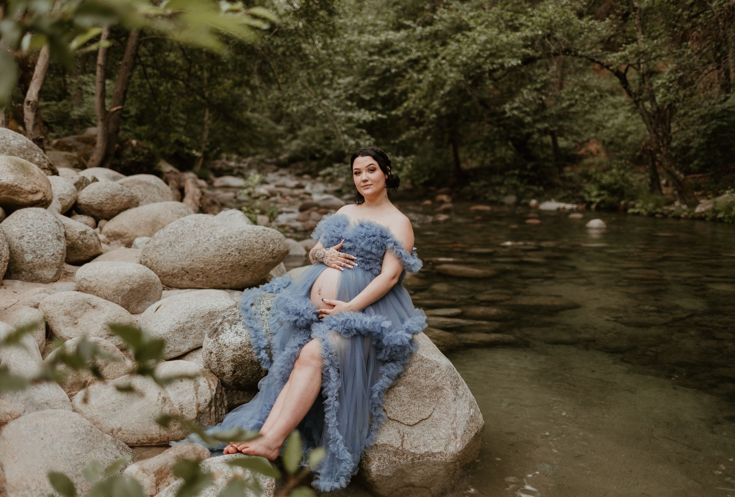 Ethereal portrait session by a creek featuring a flowing blue dress against rocky terrain.