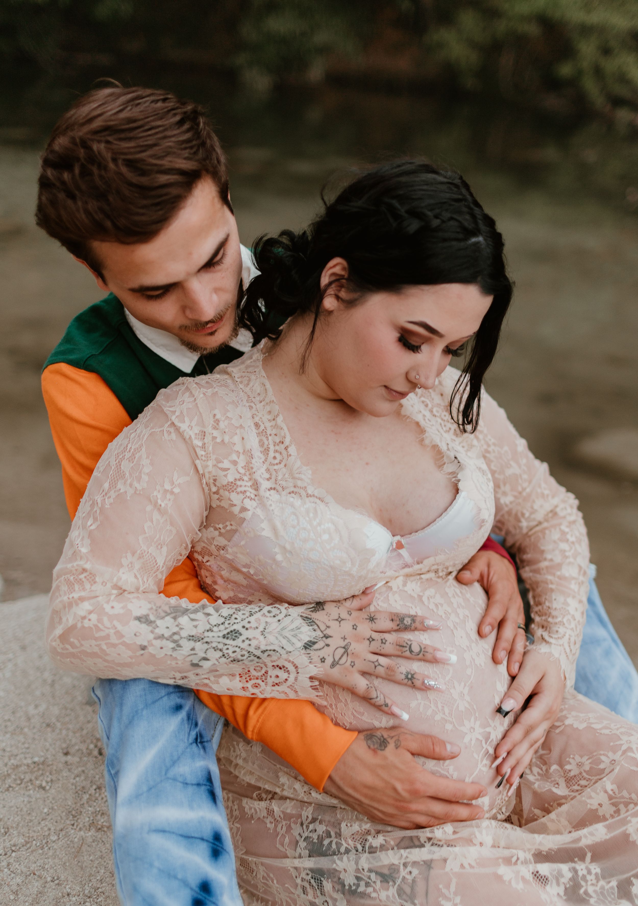 Tender maternity moment captured in natural lighting by a stream.