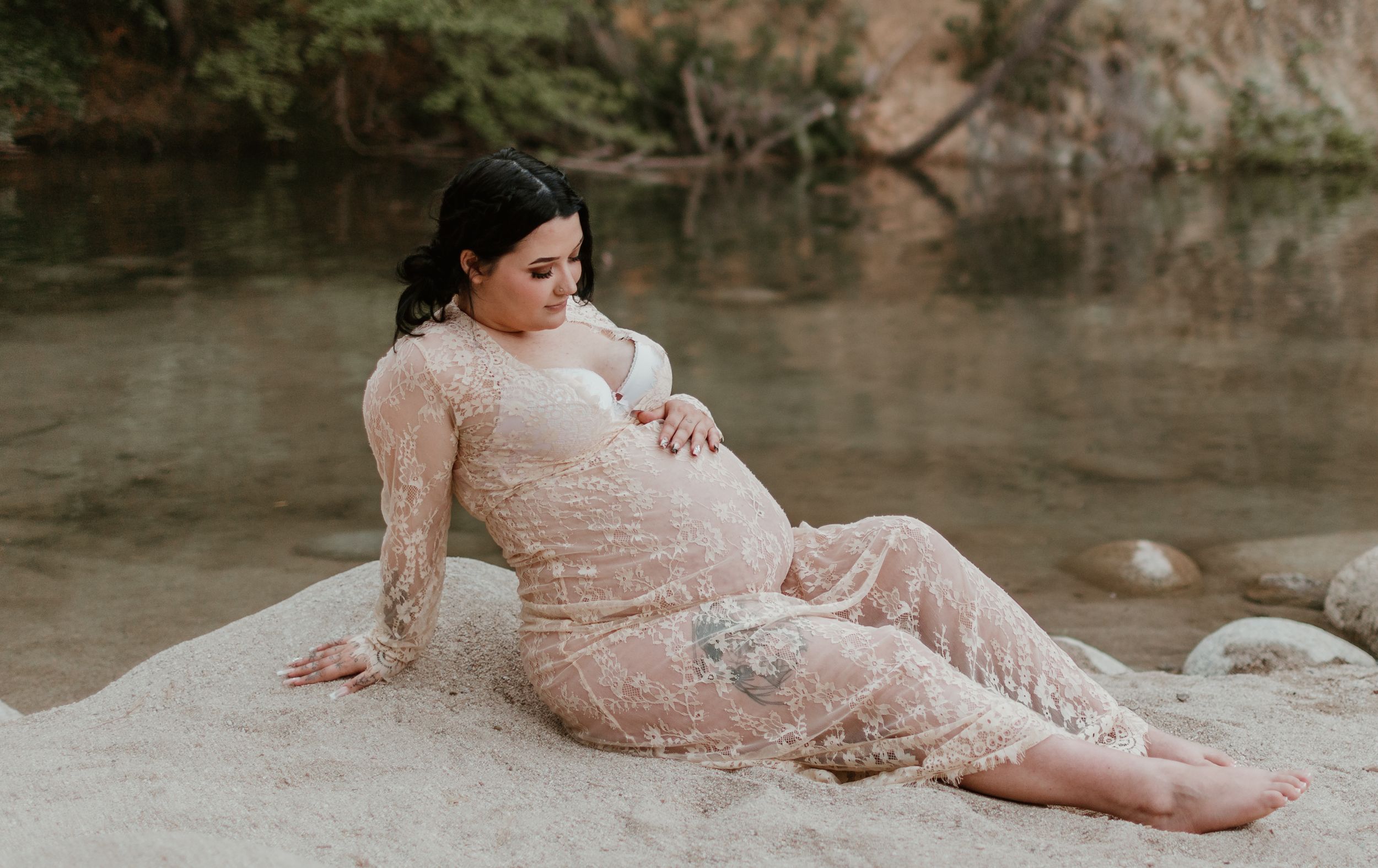 Elegant maternity photography session on rocky creek shore in lace dress.