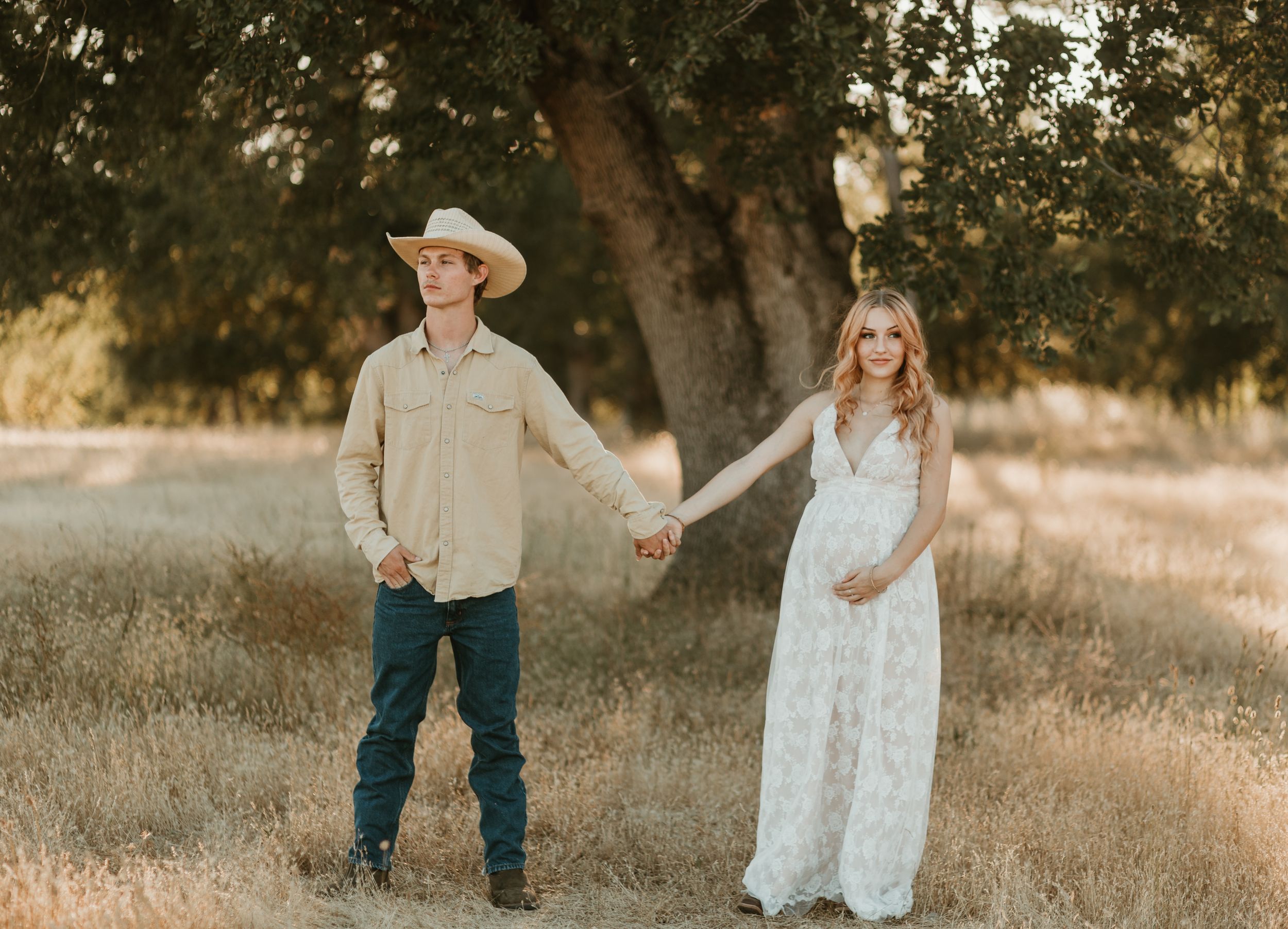 A white lace dress flows gracefully in a sun-drenched golden field with oak trees.