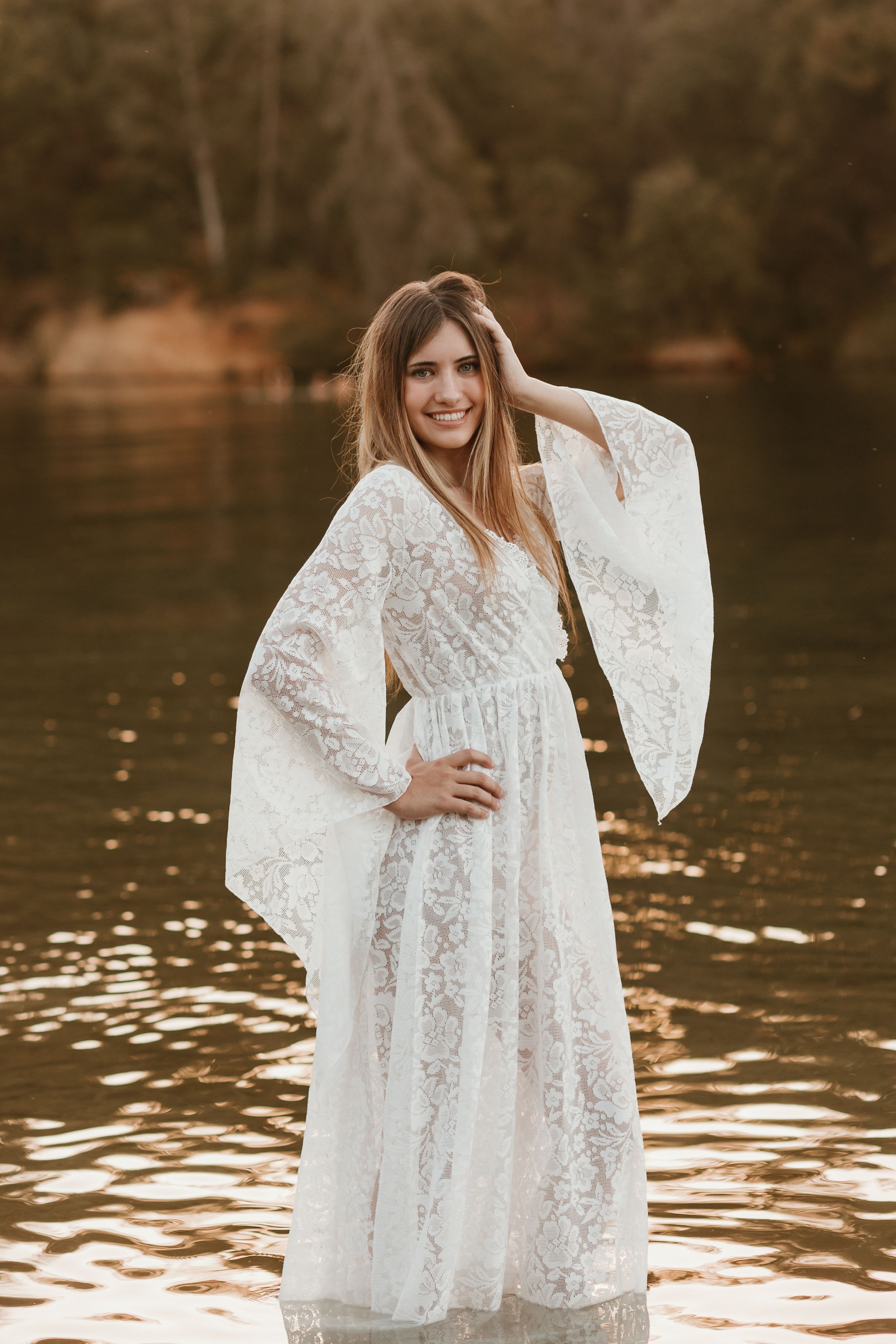 Ethereal white lace dress captures golden light reflections on water during sunset.