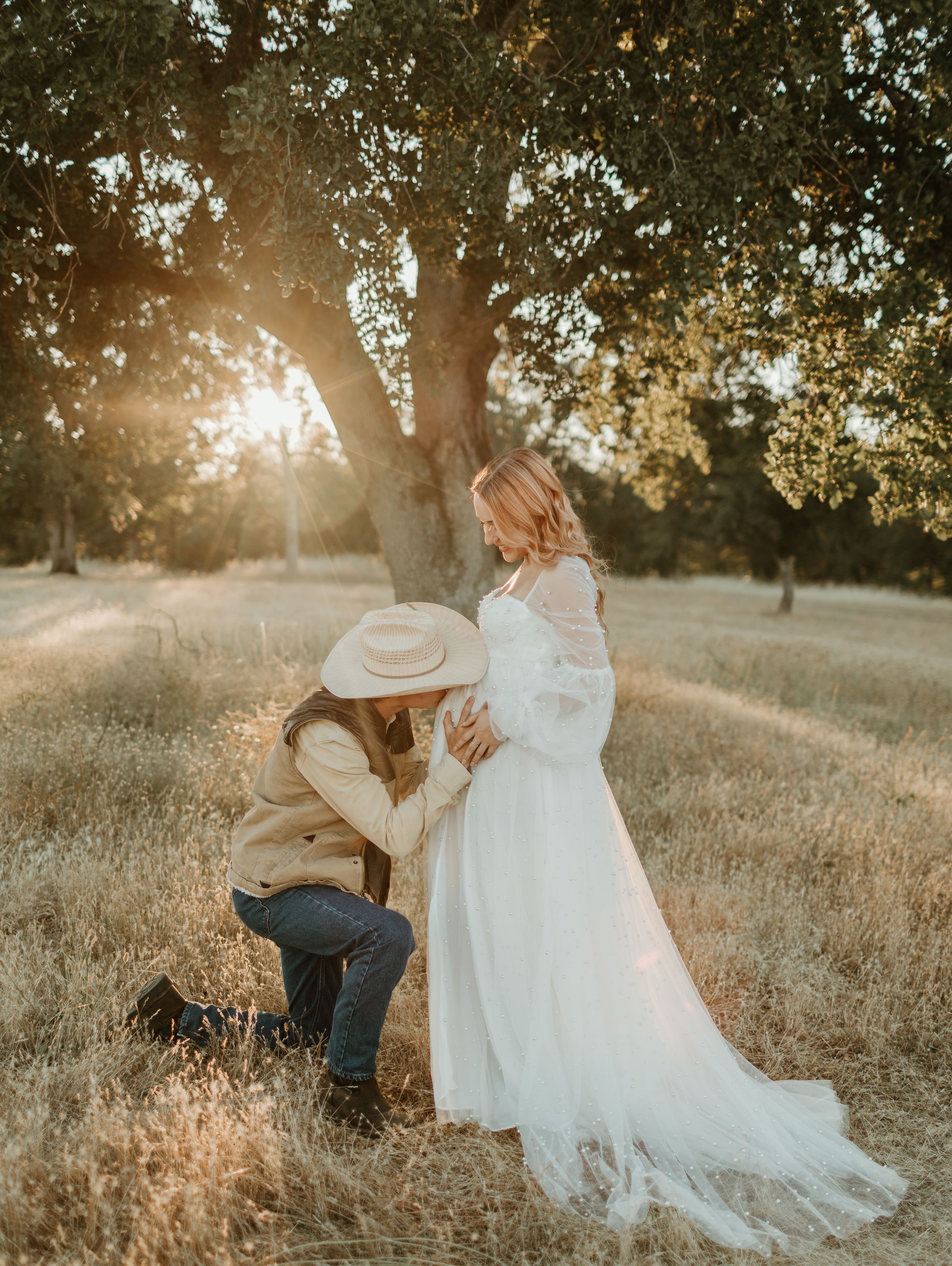 A romantic moment captured in a sun-drenched field with flowing white dress and cowboy hat details.