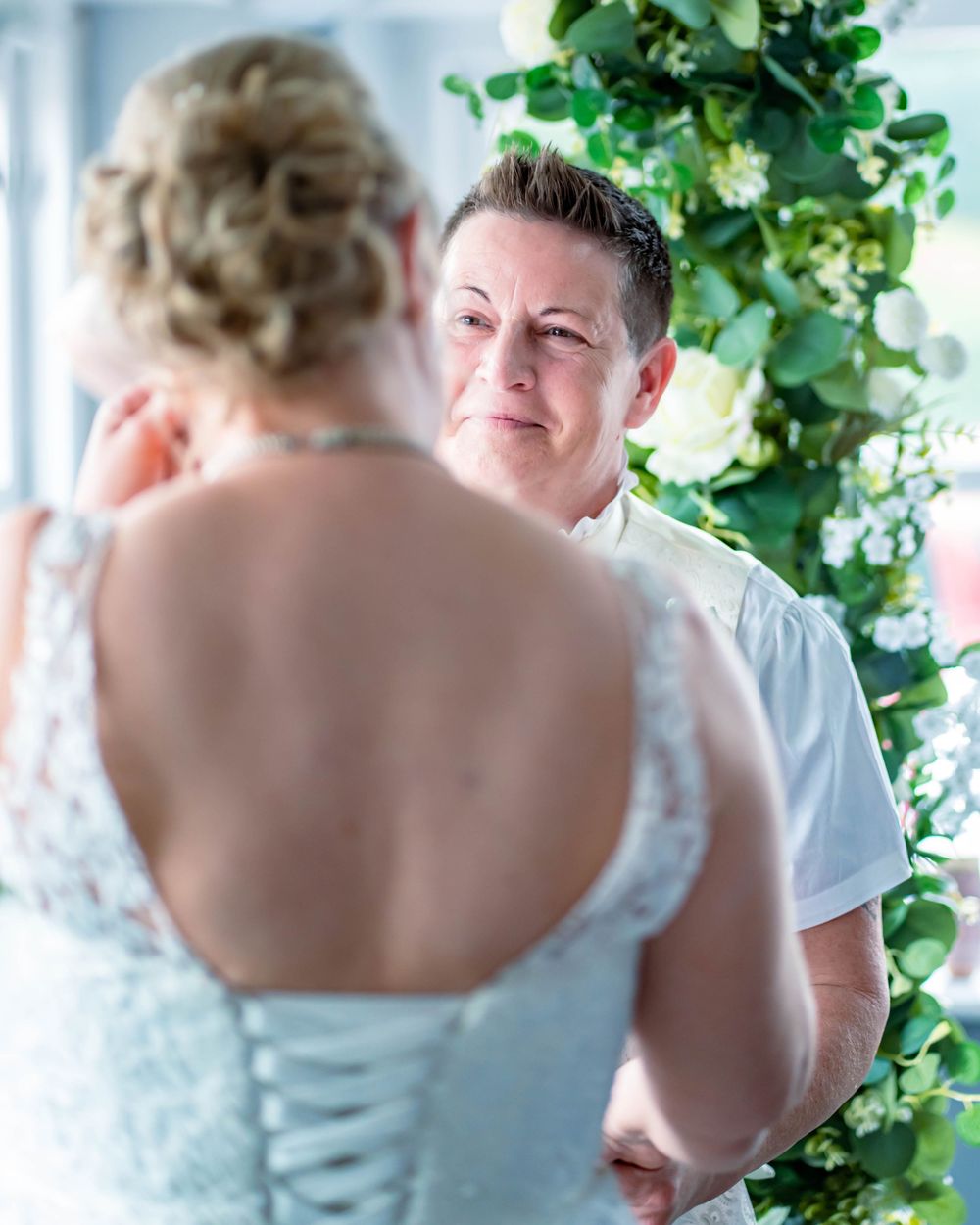 Two people share an intimate moment during a wedding ceremony with lush green foliage in the background.