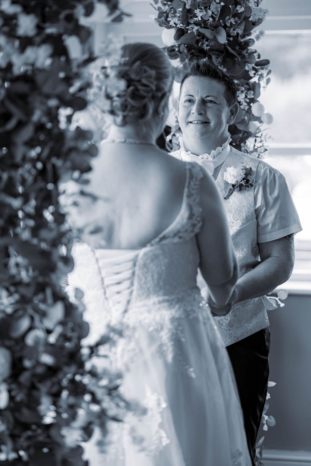 Candid moment at wedding shows interaction between two people through decorative floral arrangements in black and white.