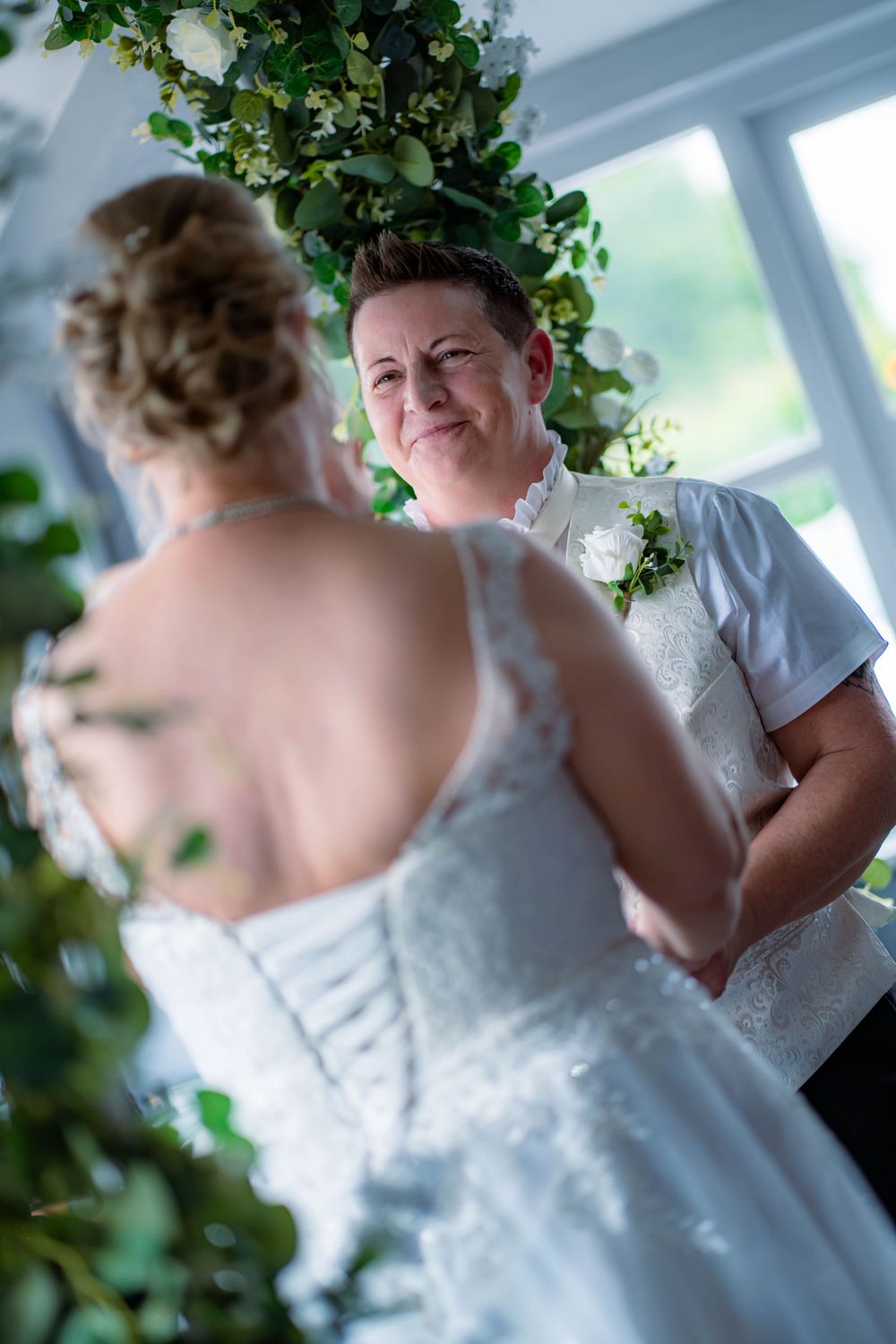 A romantic wedding scene with a couple surrounded by lush greenery and natural light in an indoor venue.