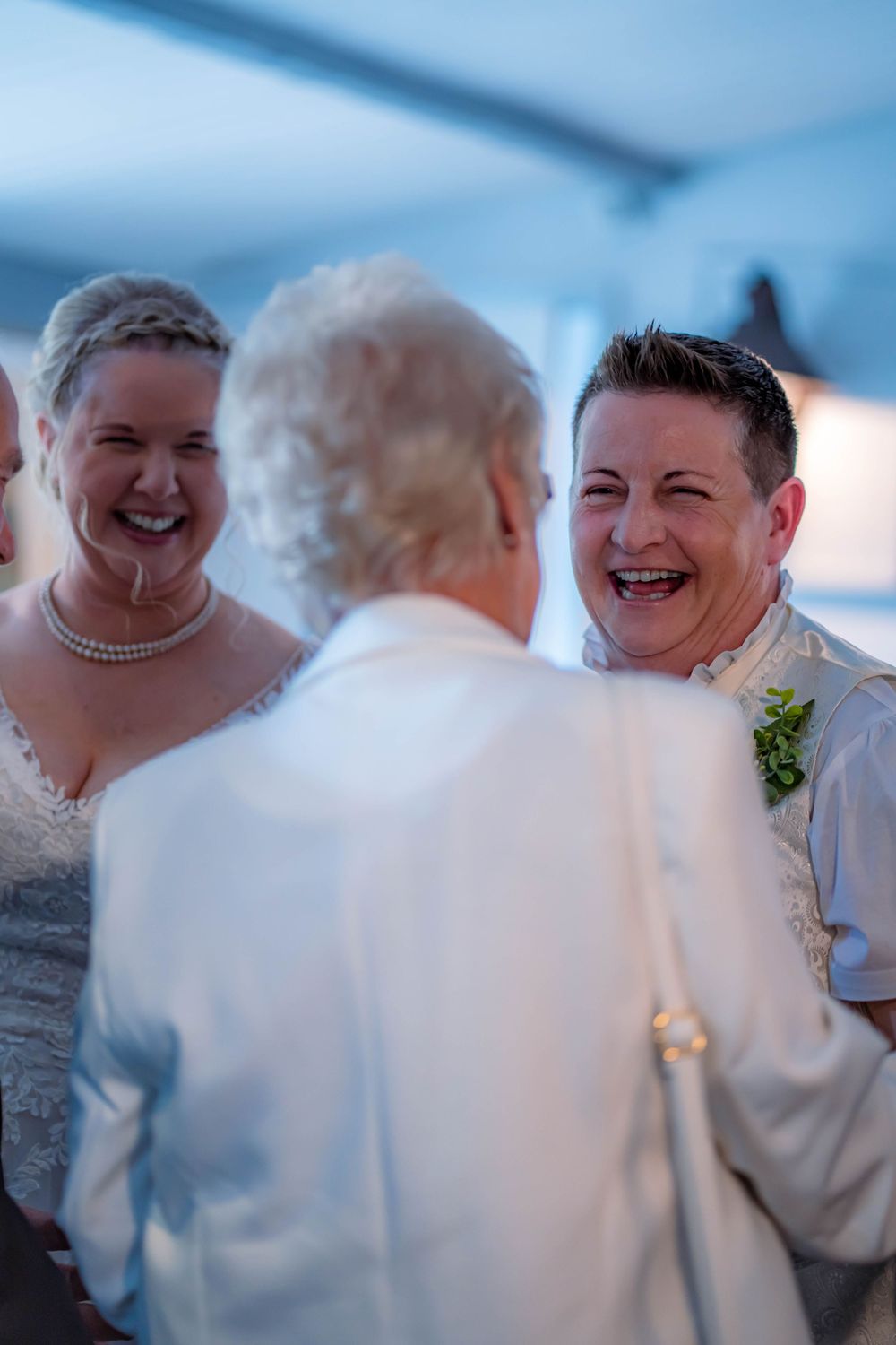 A joyful moment of laughter shared at a wedding reception between the wedding couple and a guest in white.