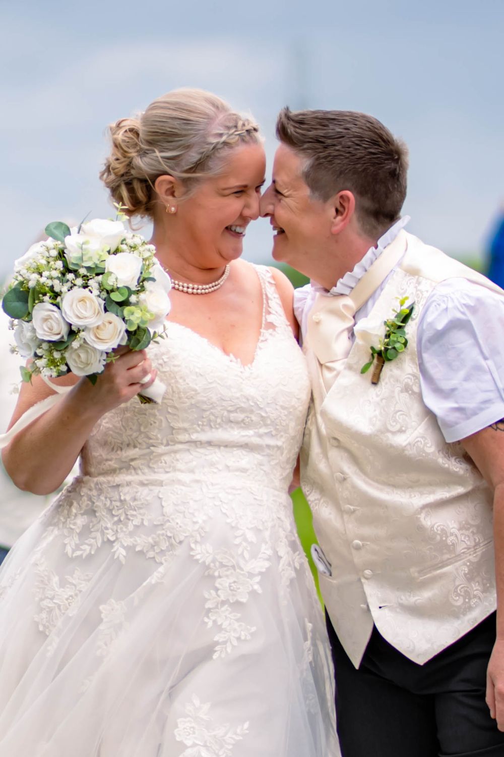 A joyful wedding couple shares an intimate moment outdoors, with the bride holding a white floral bouquet.