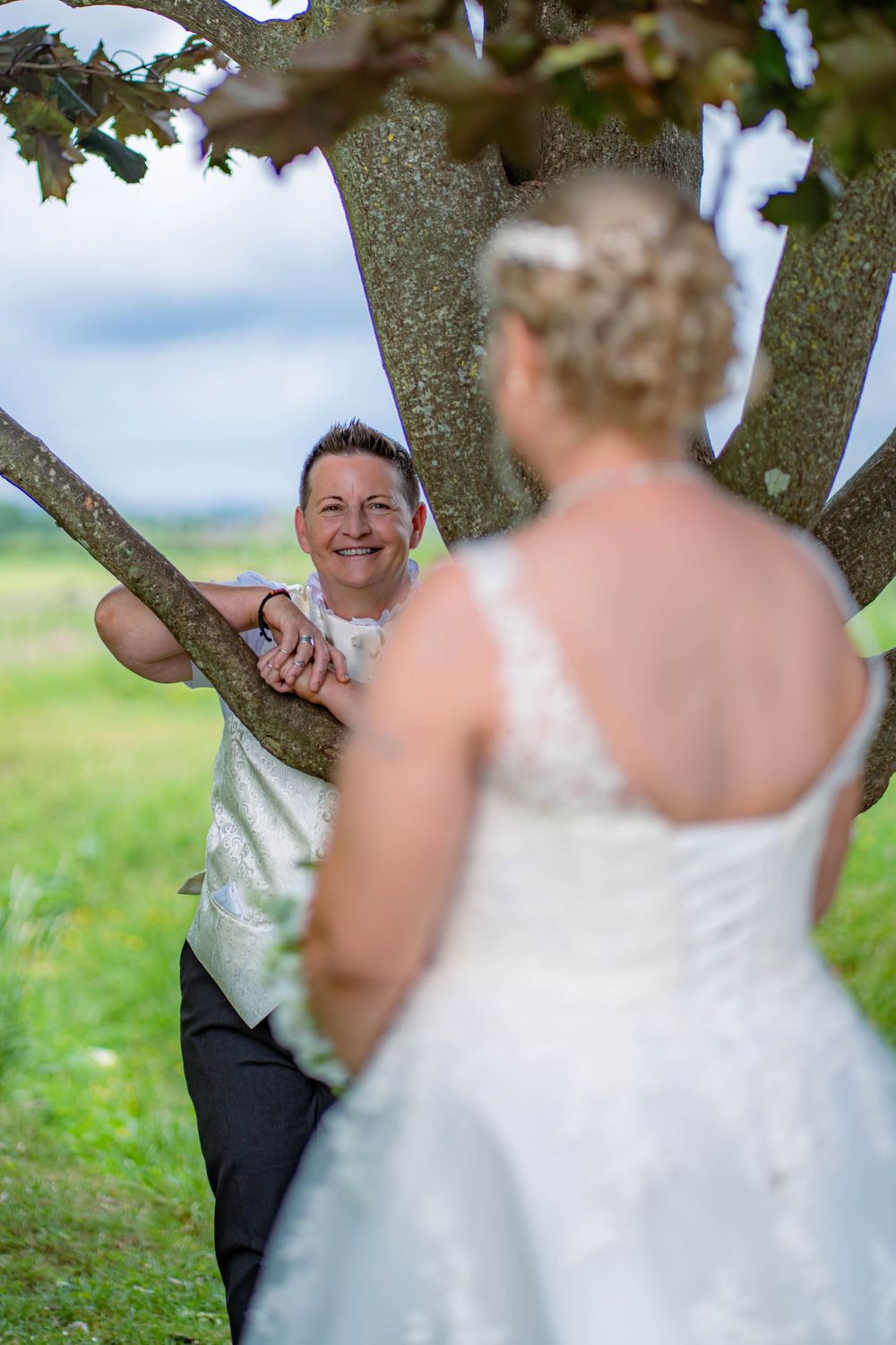 Couple sharing a romantic moment beneath a tree branch during an outdoor summer wedding ceremony.
