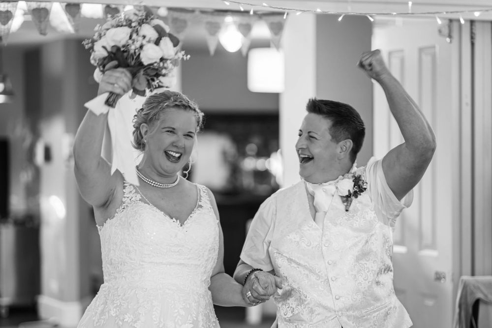 A joyful couple celebrates together at their wedding reception with raised arms and exuberant expressions.
