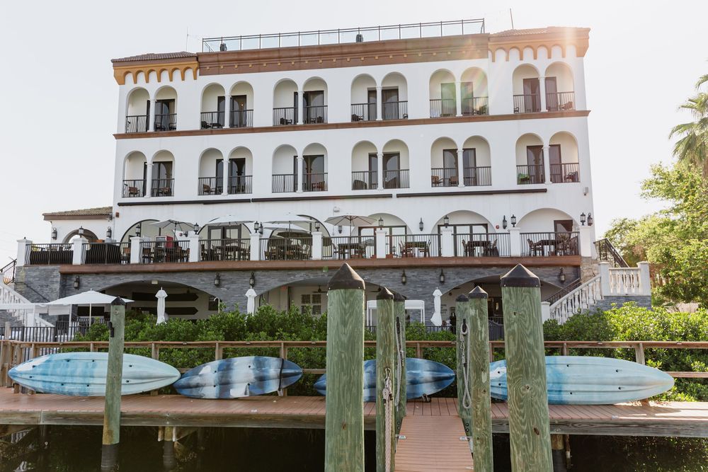 Coastal marina with wooden pilings and a white Mediterranean-style building with ornate balconies in the background.
