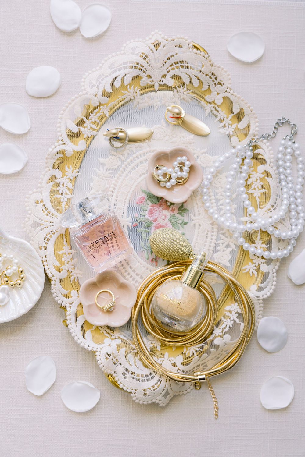 Wedding accessories including rings, pearls, perfume, and delicate lace on an ornate gold-trimmed decorative tray.