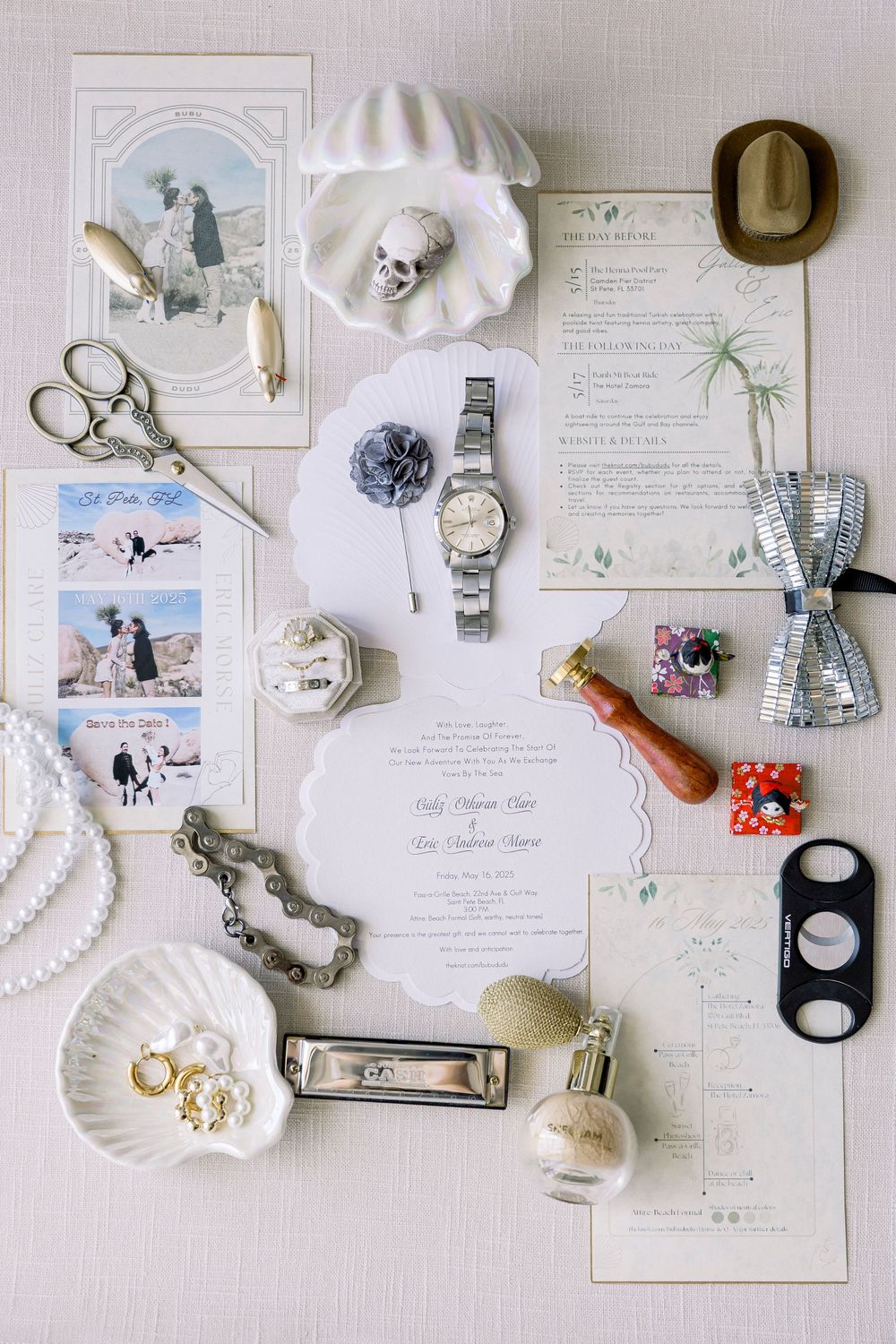 Flat lay of vintage wedding details including invitations, jewelry, watch, scissors and floral elements on white background.