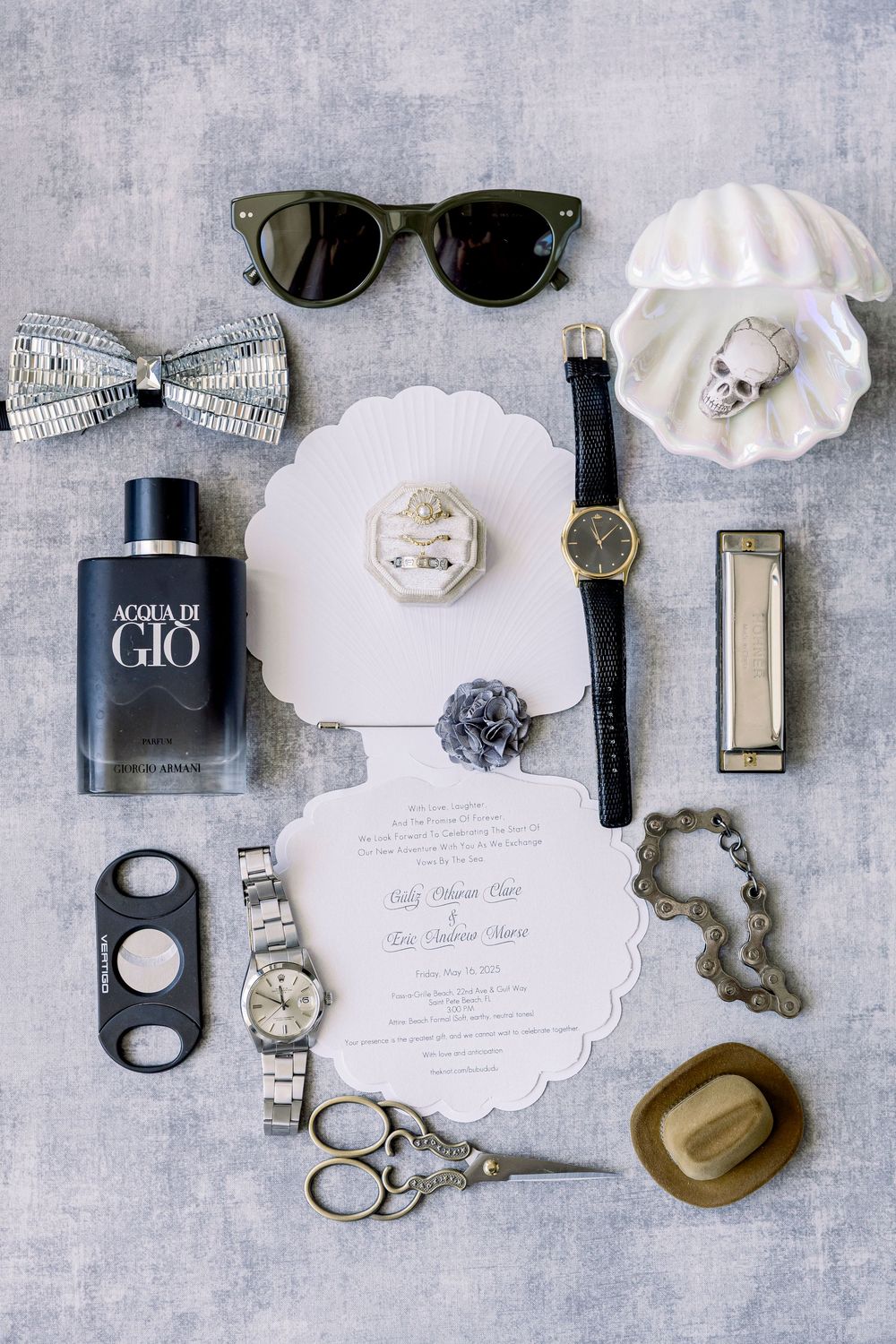 Wedding accessories flat lay with sunglasses, perfume, watches, bow tie and invitation on gray background.