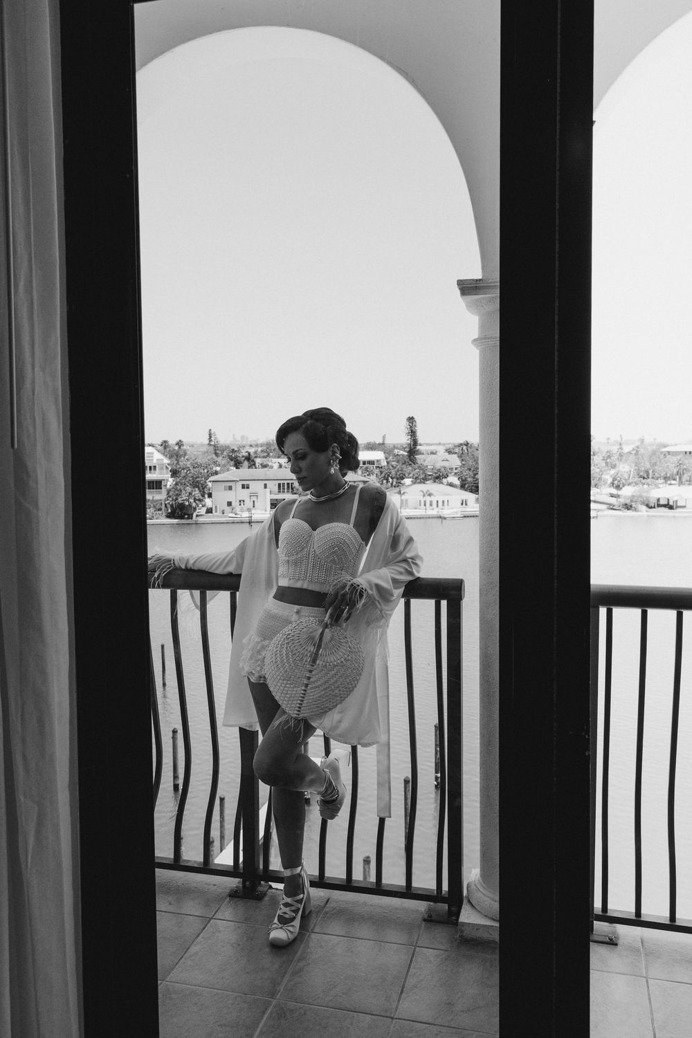 Artistic black and white photo of a terrace overlooking a waterfront cityscape through an arched doorway.