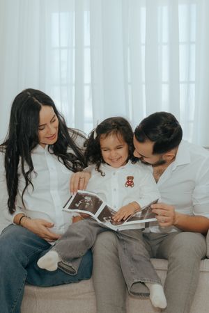 Happy family sitting together on couch looking at ultrasound images and smiling while sharing special moment.