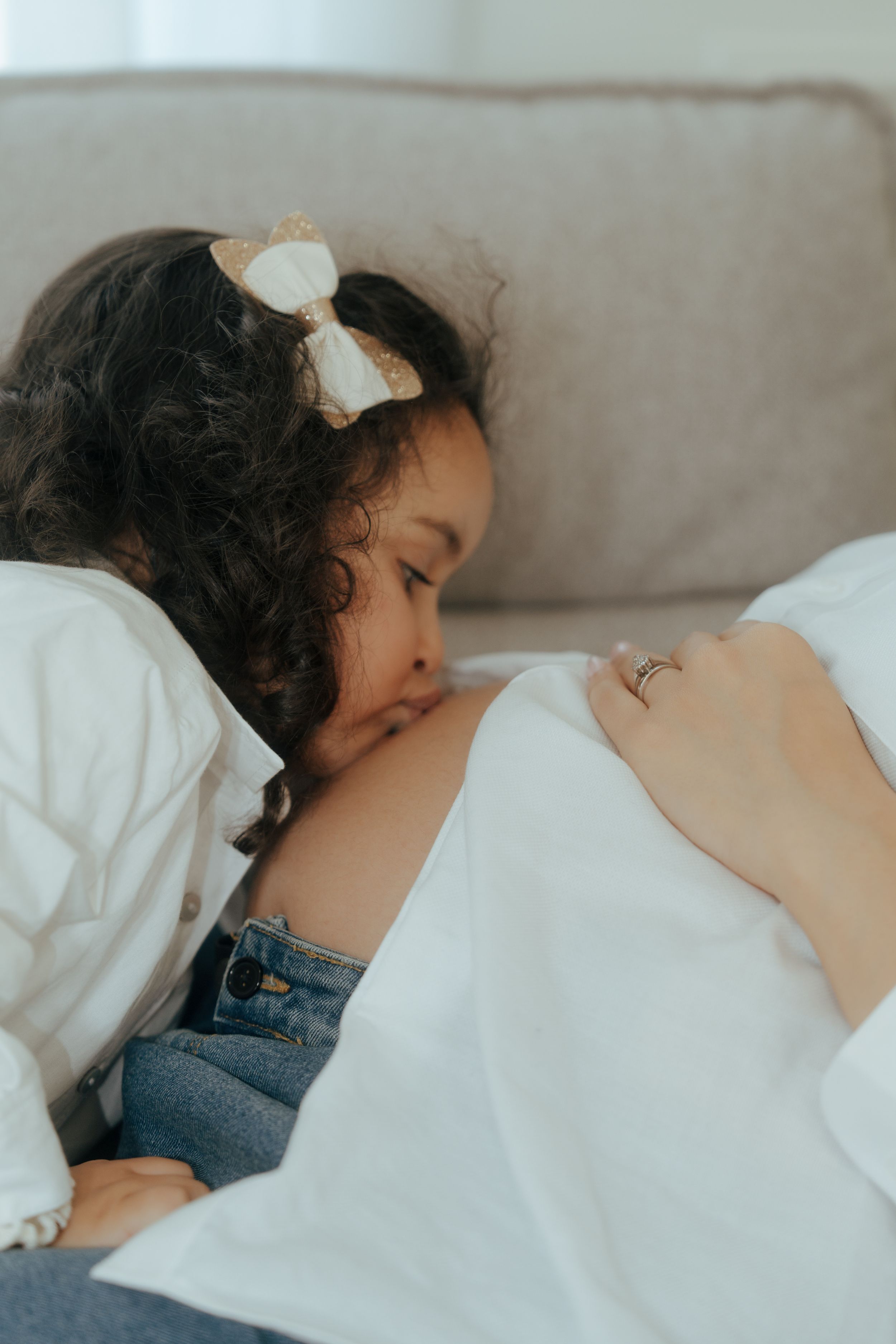 A small child rests peacefully on a white pillow while wearing a white bow and denim outfit.
