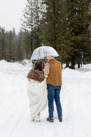 snowy winter elopement in Idaho City couple facing back under clear umbrella kissing