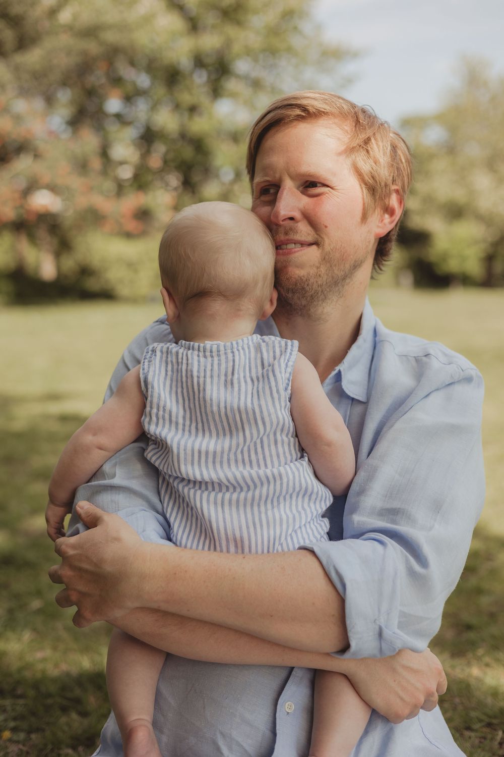 a father (dad) holds his baby to his chest on a sunny day in an outdoor park