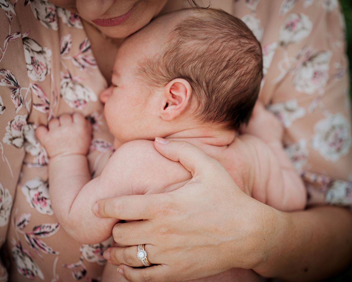 Newborn baby sleeps peacefully against floral fabric while being held.