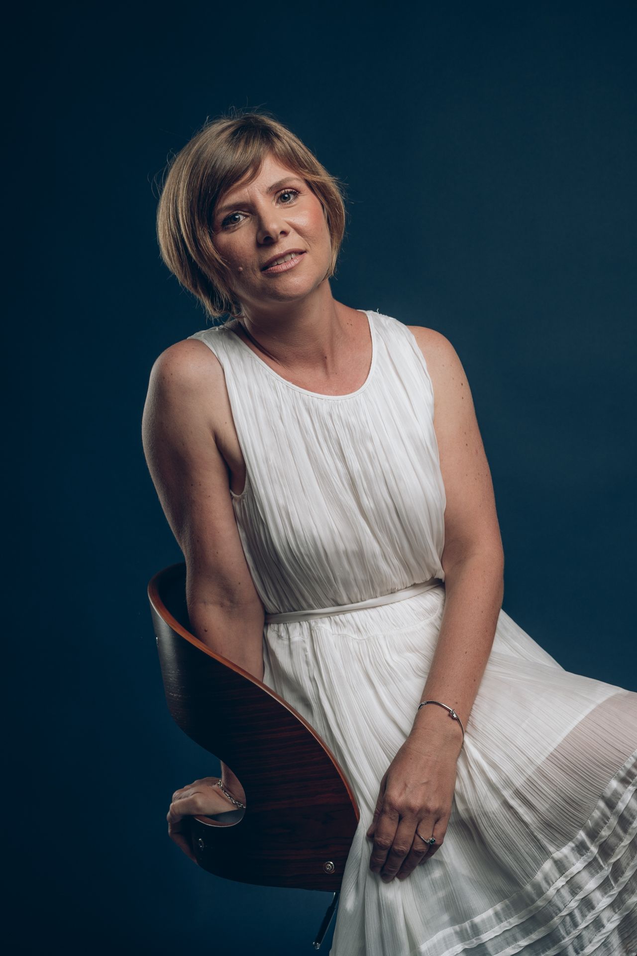Studio portrait of a person in a flowing white dress seated against a dark background.