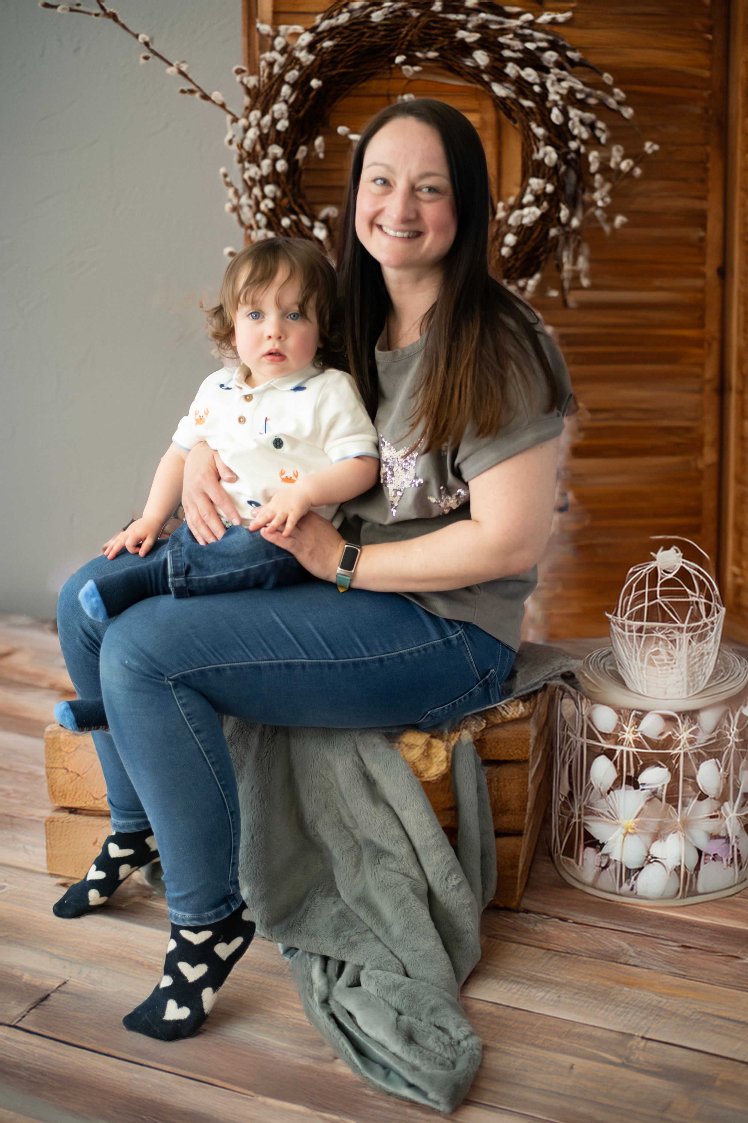 A heartwarming indoor portrait showing an adult and toddler sitting together against a wooden wall with spring decor.