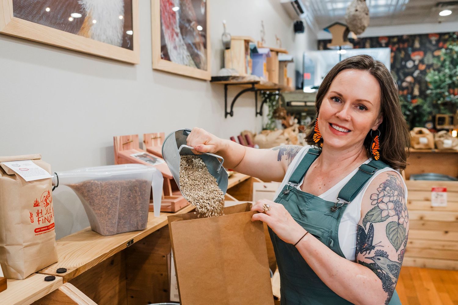 Artisan wearing green overalls scoops grains at workbench in studio workspace with warm lighting and natural decor.