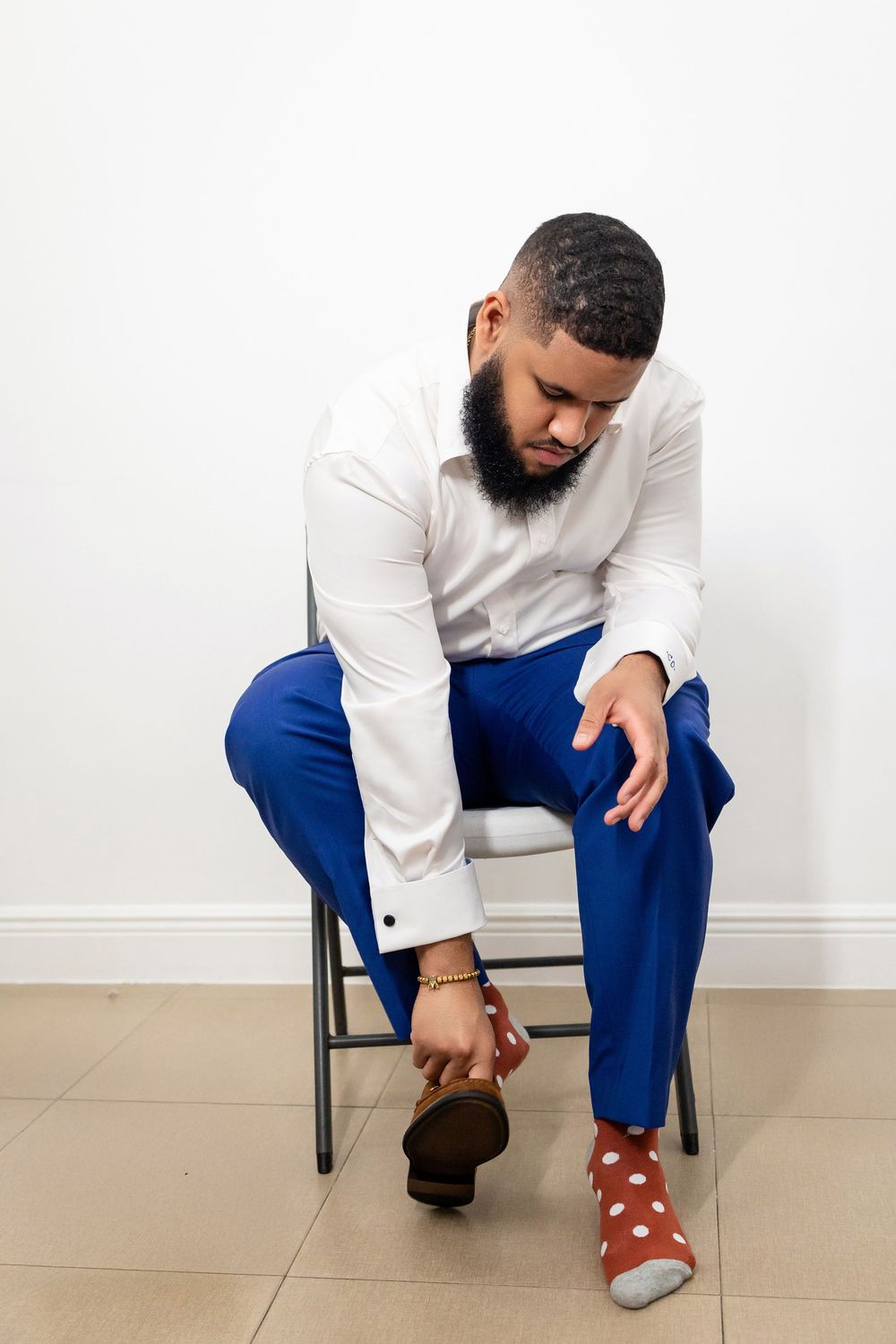 A person in a white shirt and blue pants sits on a chair adjusting their polka dot socks and brown shoes.