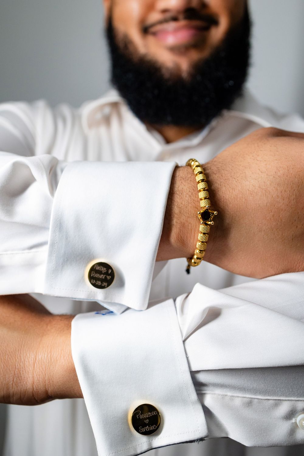 Close-up of crisp white dress shirt with gold cufflinks and a gold beaded bracelet on wrist.