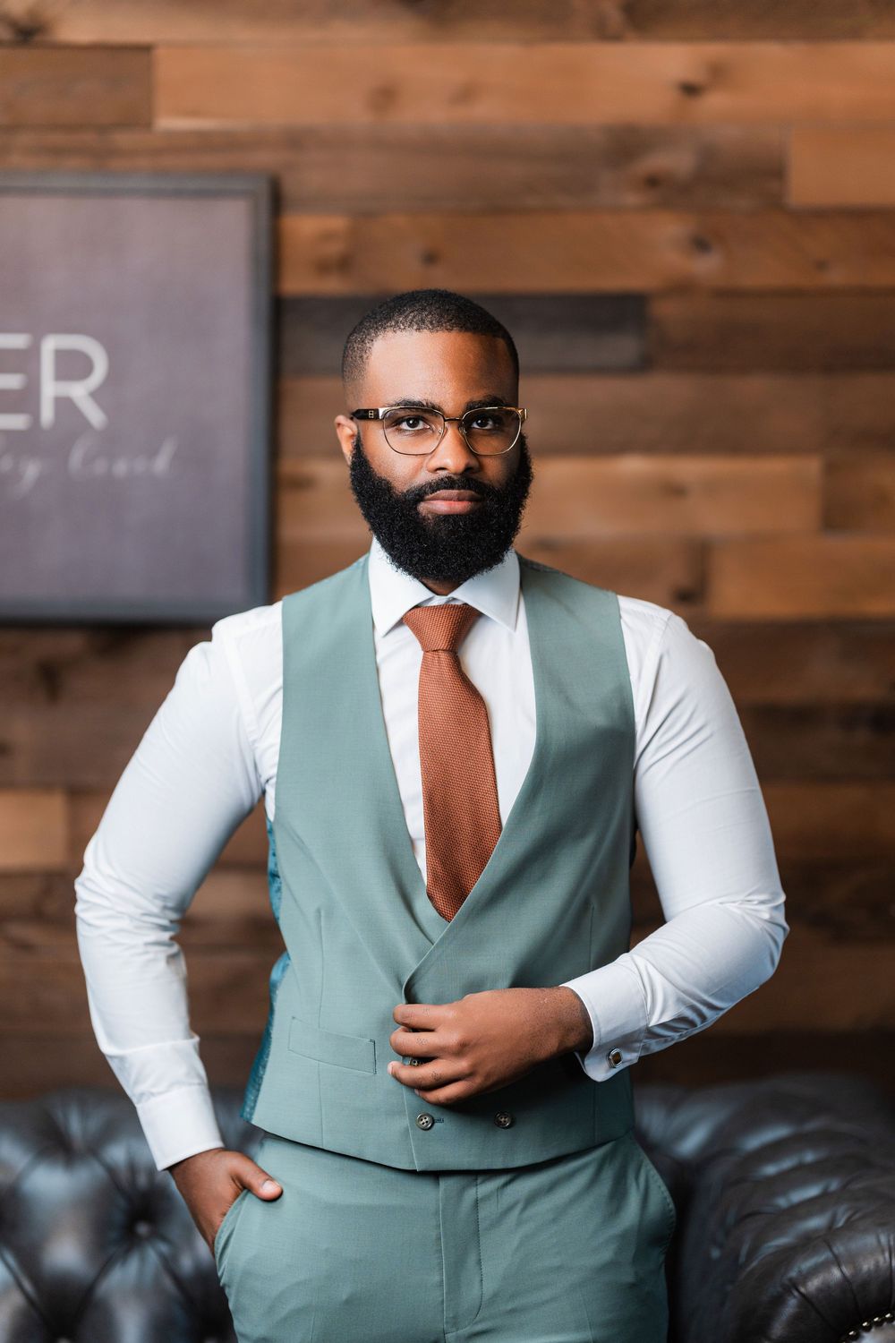 Stylish dresswear featuring sage green vest, copper tie and white dress shirt against wooden wall background.