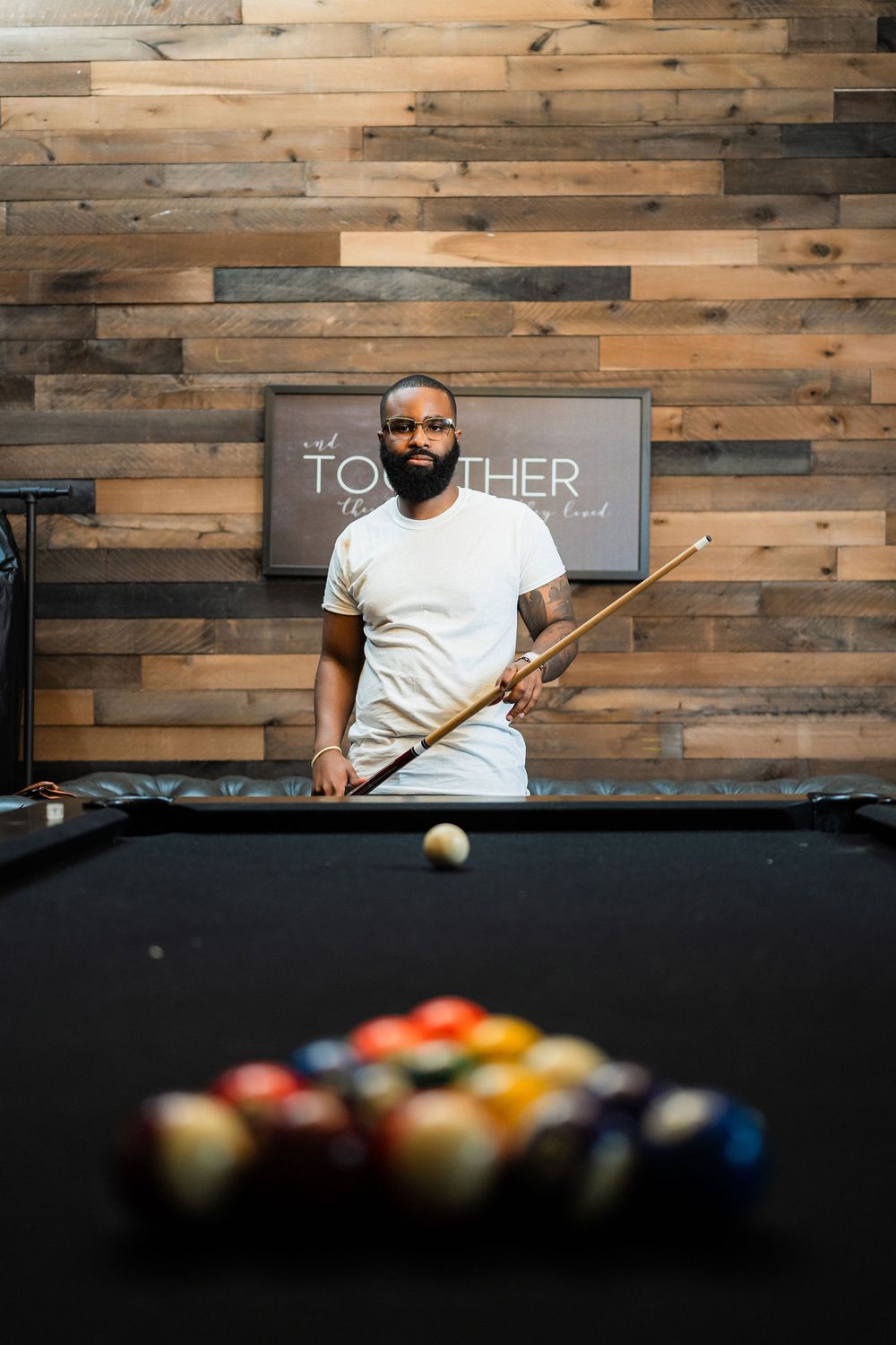 A pool player lines up a shot on a billiards table with rustic wood paneled walls in the background.