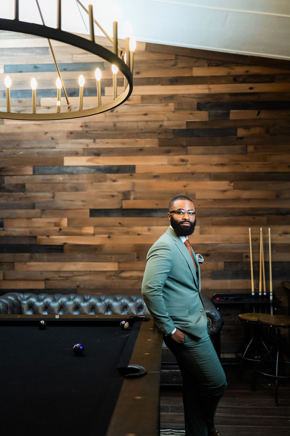A stylish mint green suit ensemble photographed in a room with wood walls and pool table under circular lighting.