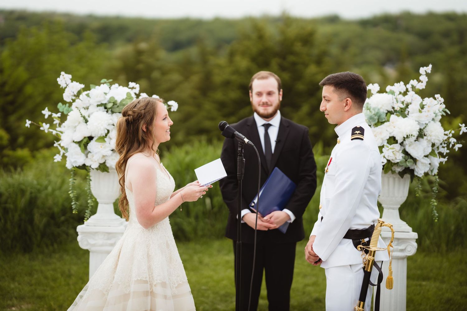 A romantic outdoor wedding ceremony surrounded by lush greenery and white floral decorations at sunset.