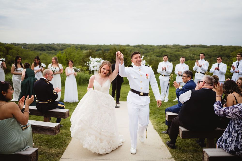 A joyful couple celebrates with raised arms while walking down the outdoor aisle at their beach wedding ceremony.