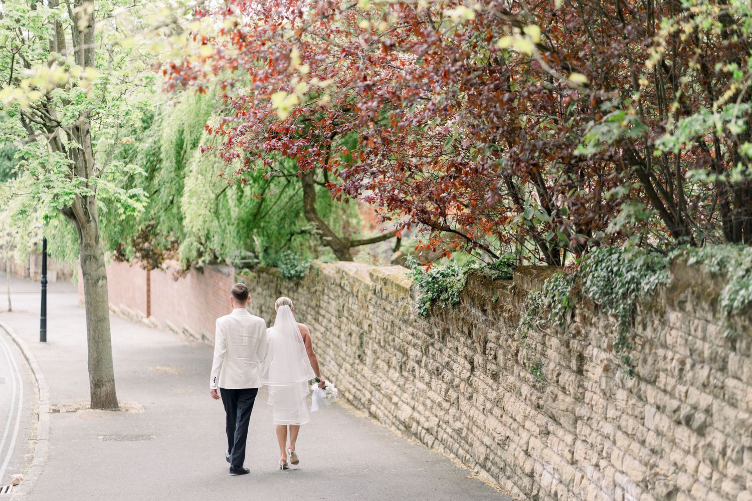 Candid shot of newlyweds walking together in the leafy Park Estate, Nottingham, showcasing relaxed wedding photography with soft light.