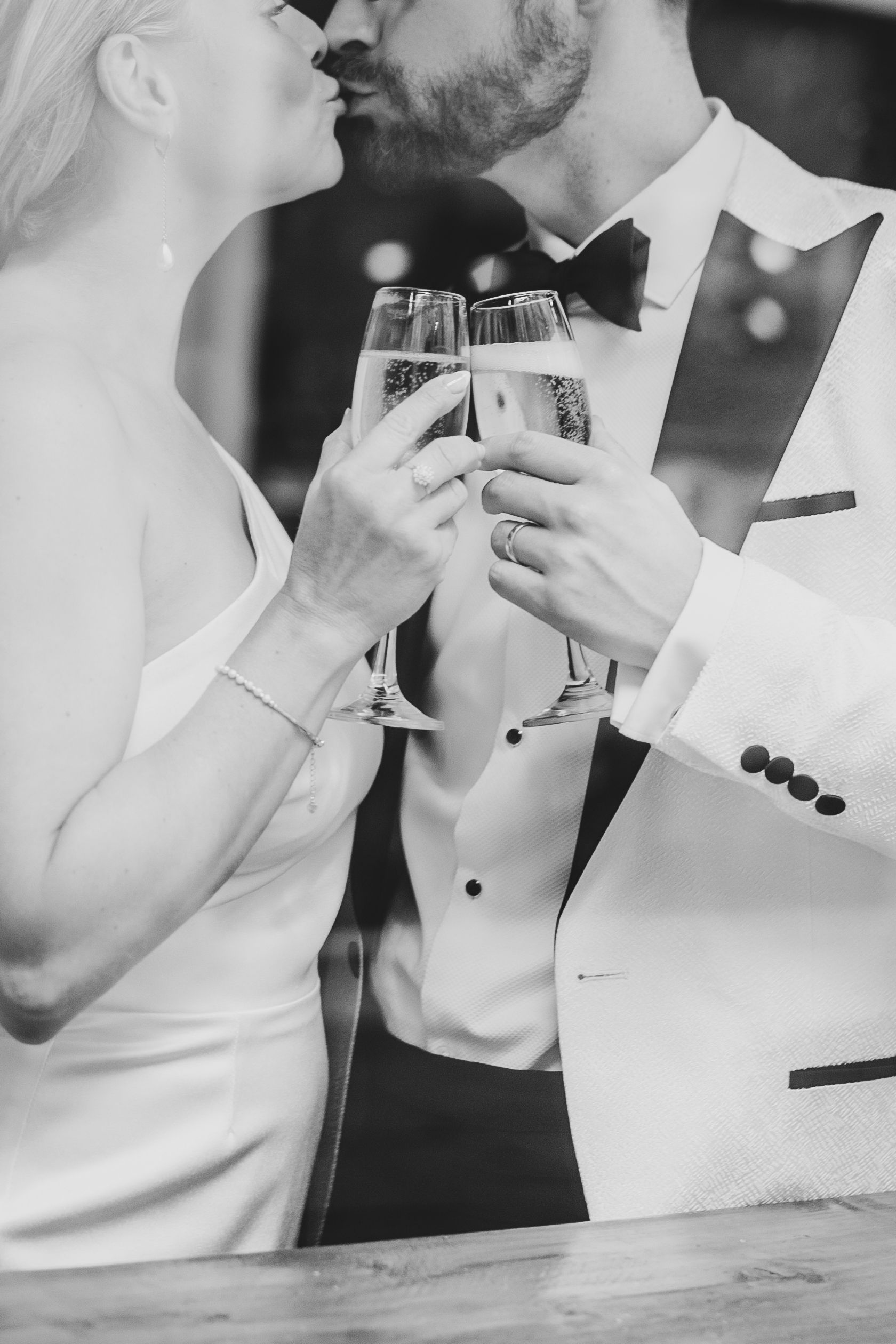 Black and white close-up of bride and groom kissing, toasting champagne at Bar 47 during spring elopement wedding in Nottingham city centre.