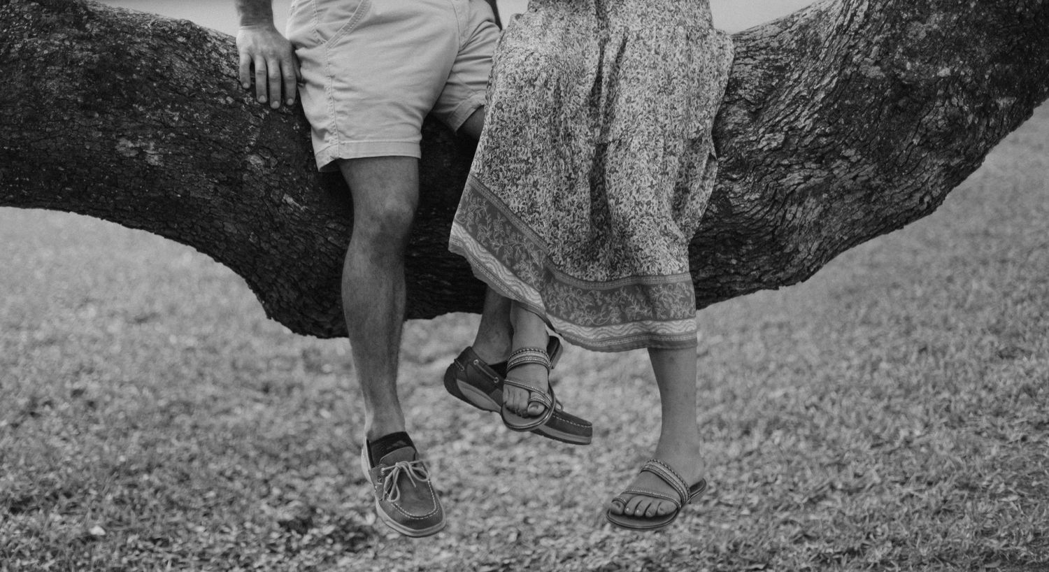 Black and white photo showing feet and legs of two people standing on tree roots.