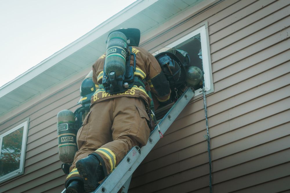 Firefighter climbing ladder to rescue during training exercise wearing protective gear and oxygen tank.
