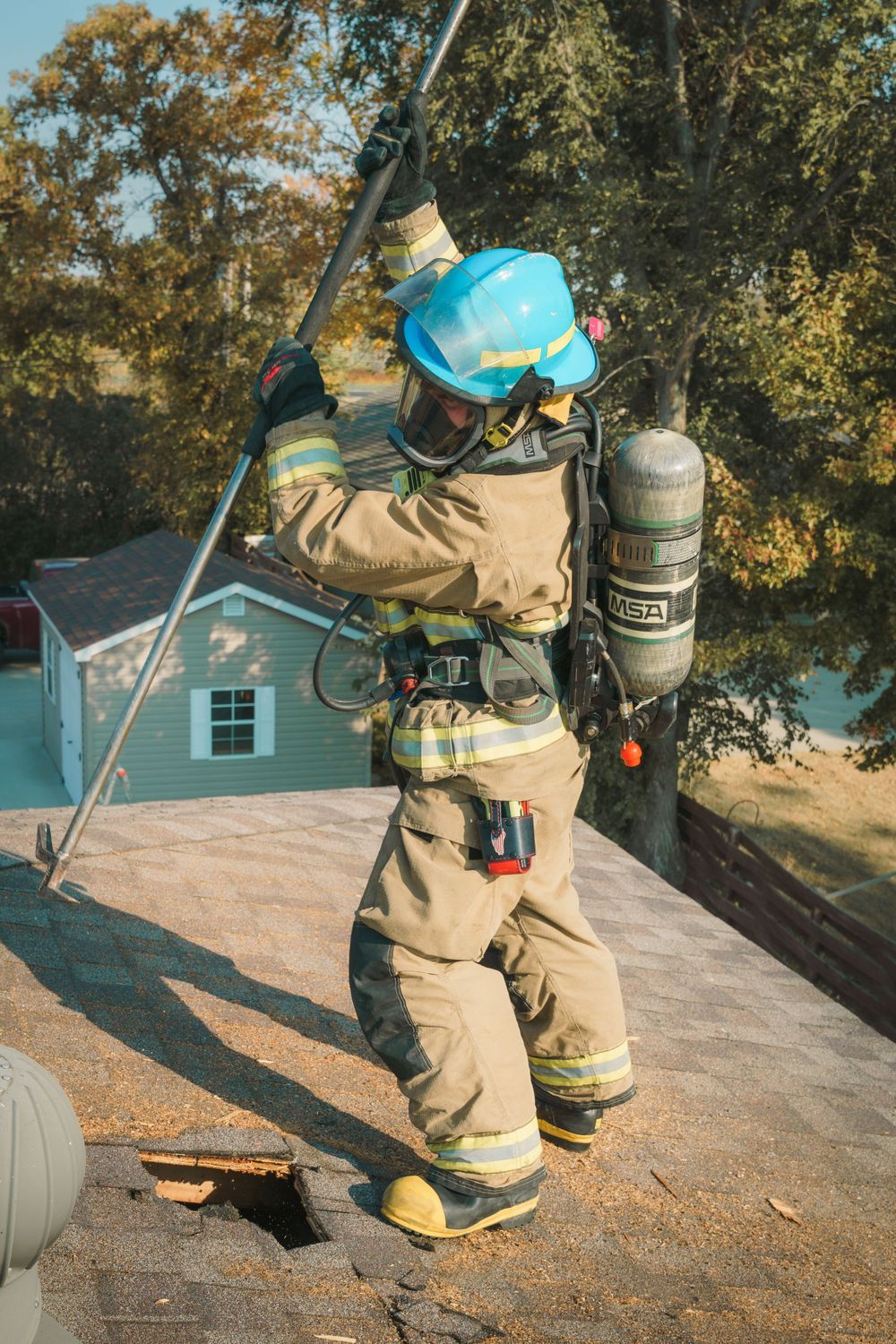 A firefighter in protective gear works on a residential rooftop with safety equipment and tools during a response call.