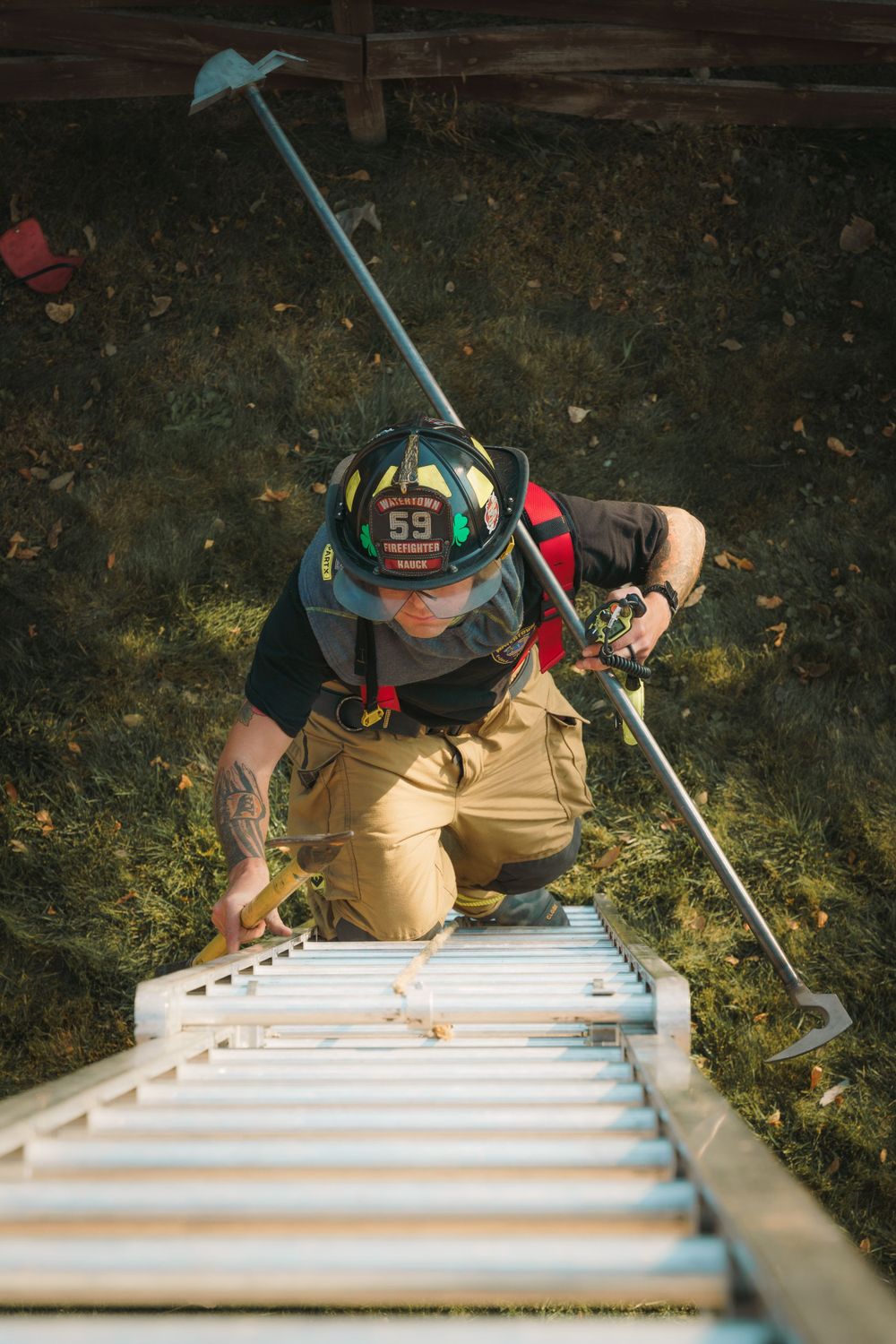 Looking down from above at a firefighter in protective gear climbing a tall ladder during training exercises.